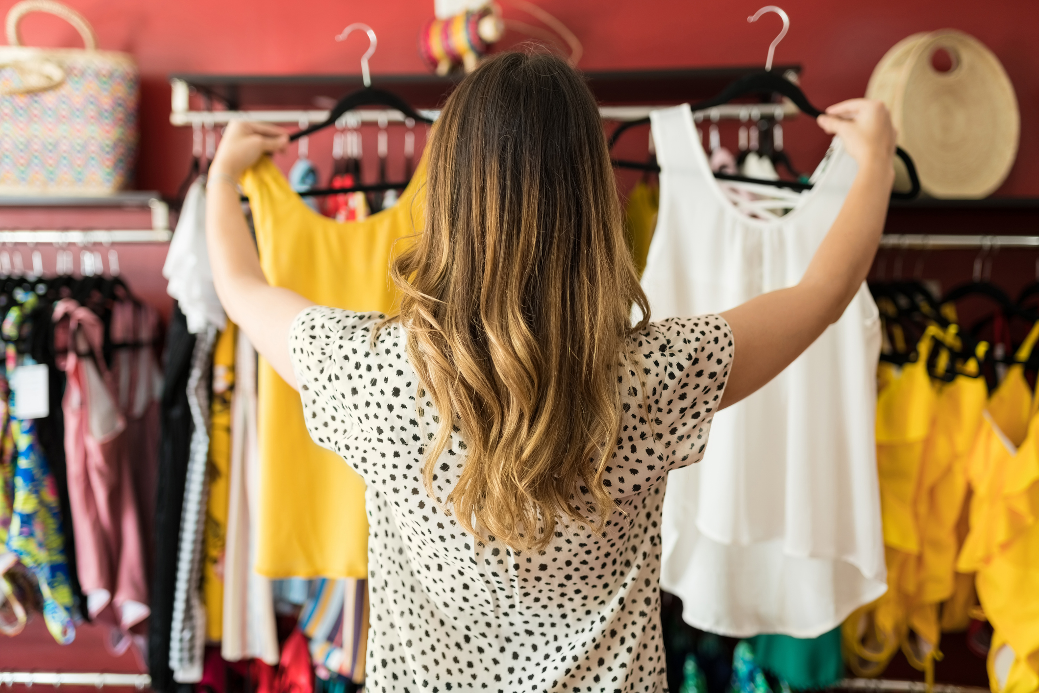 Backside of Woman Comparing Two Sleeveless Tops, in a Colorful Clothing Store
