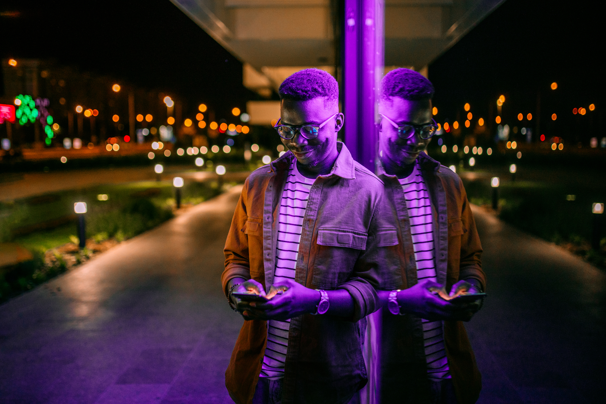Smiling Young Man on His Smartphone, Purple Light, in a City During the Night