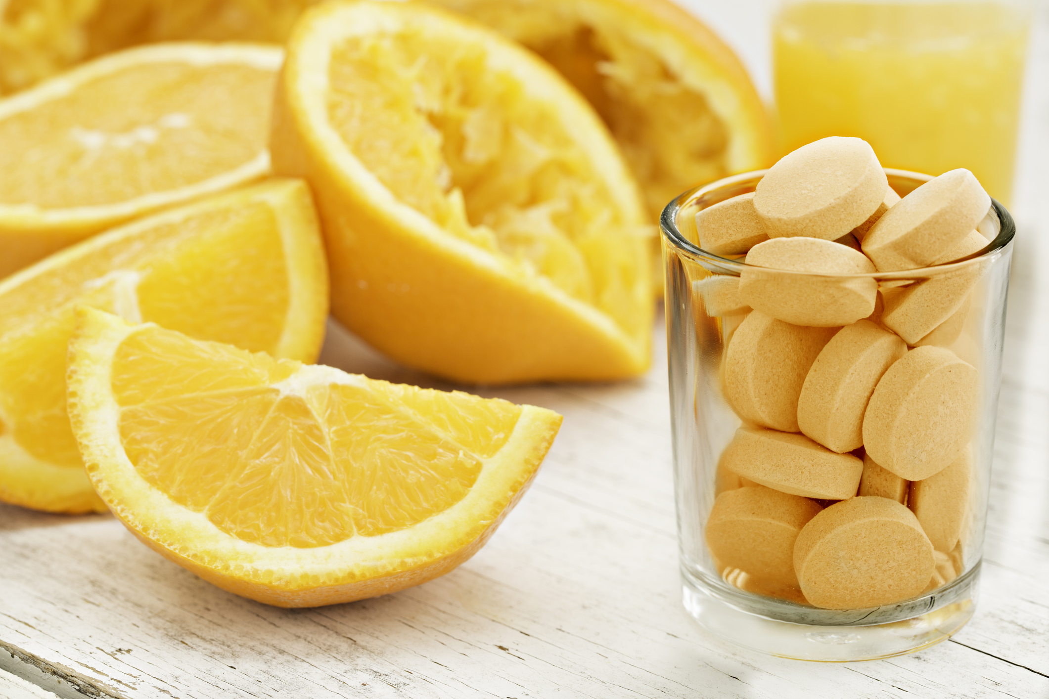 Small Glass Filled With Vitamin C Chewable Tablets Next to Several Slices of Oranges