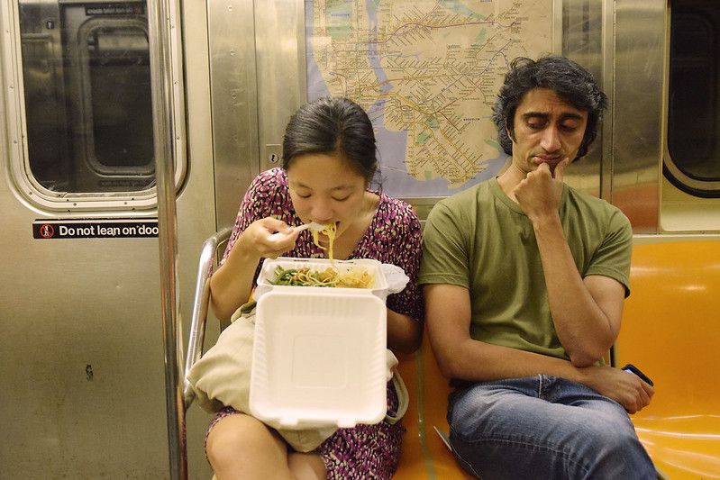 Woman Eating Takeout on Subway While Man Gives Side Eye