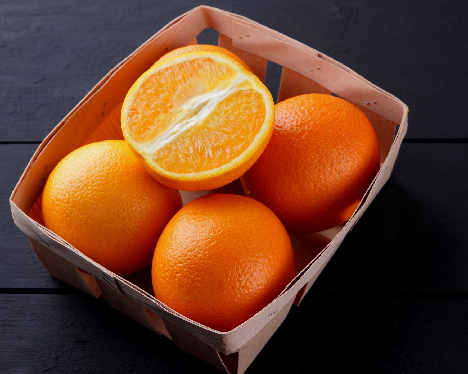 Four whole oranges in box topped with one half of a cut orange