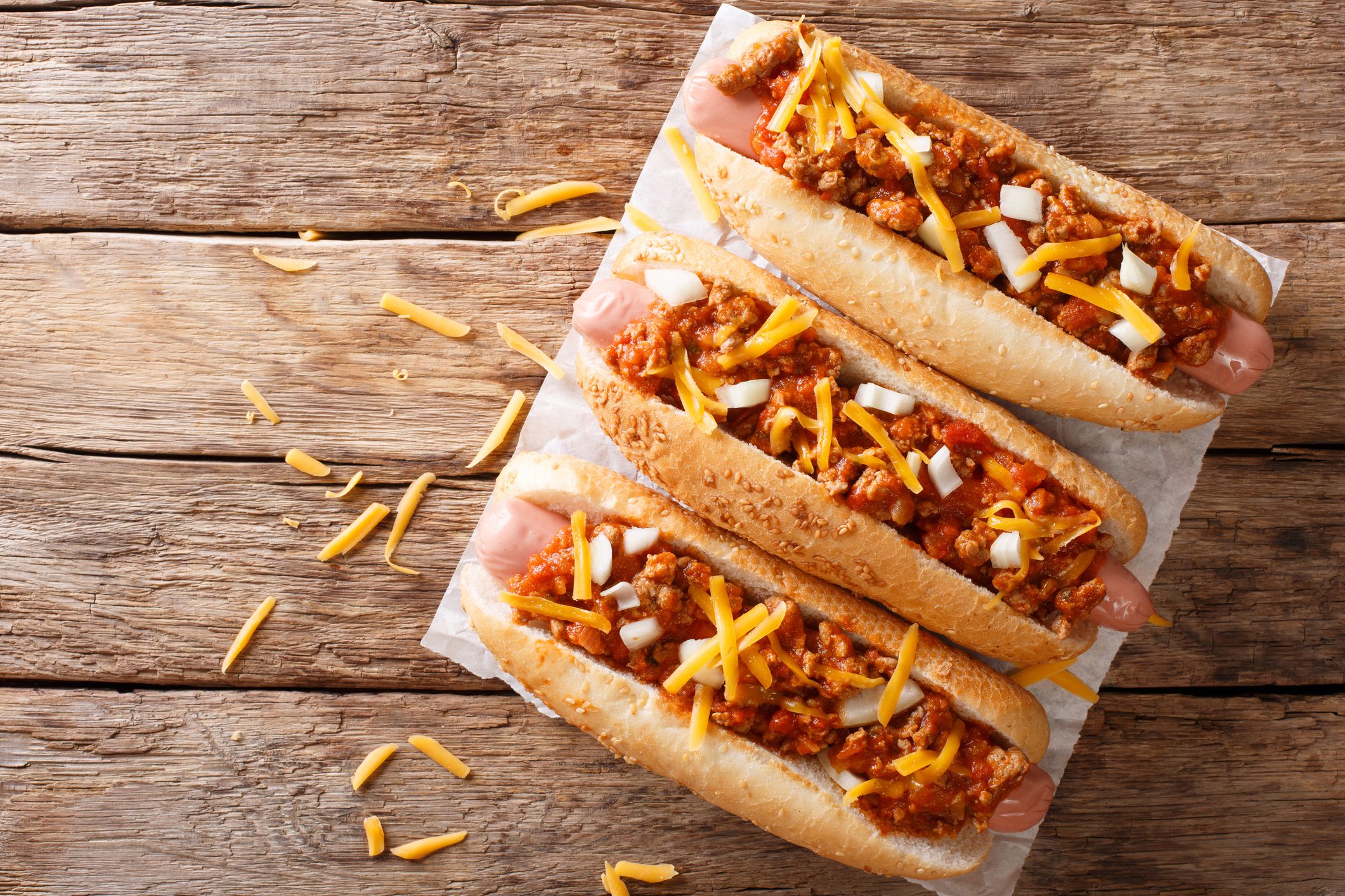 Traditional American chili hot dogs with cheddar cheese, onion and spicy sauce closeup on the table. horizontal top view from above