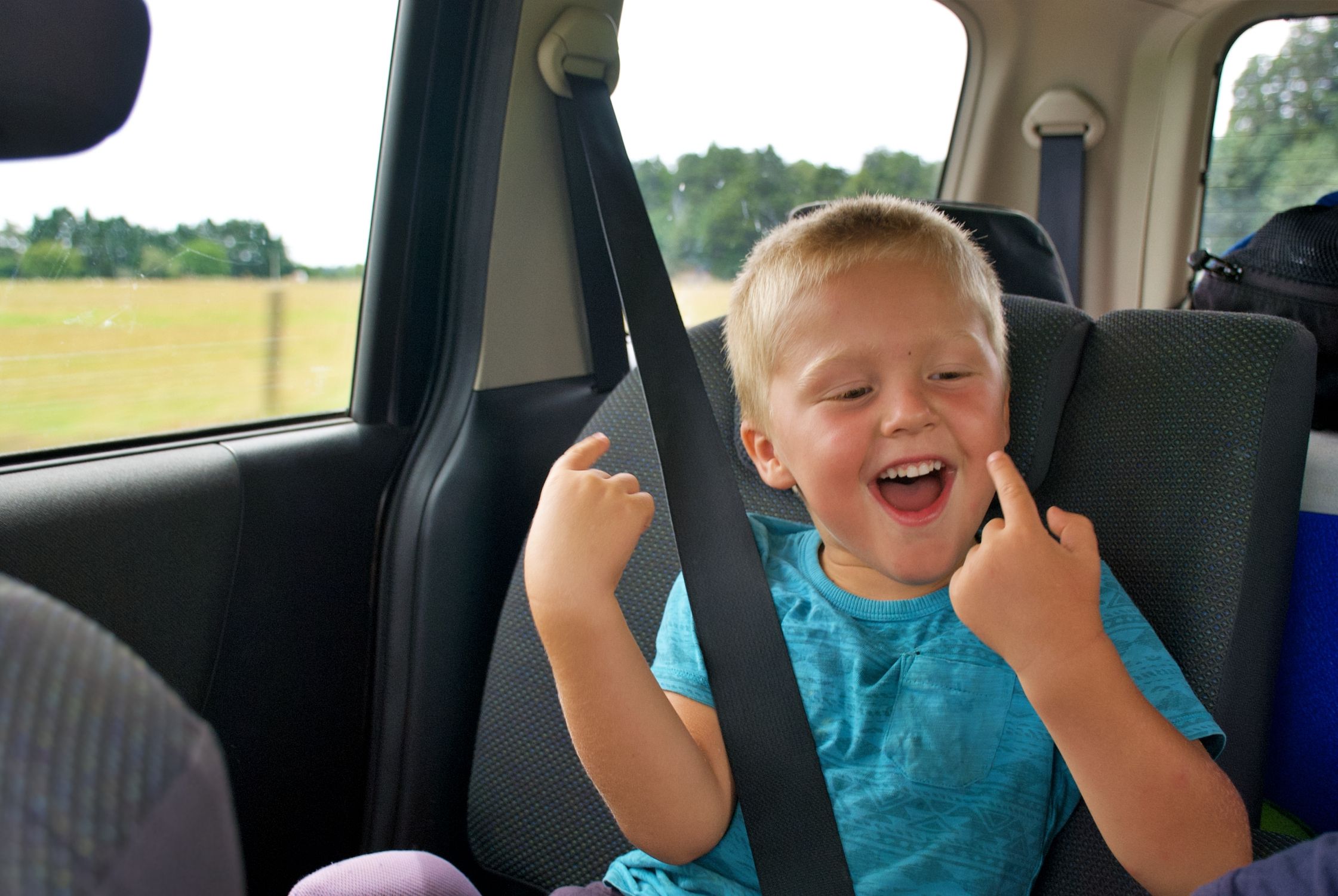 Looking to the back car seats whilst travelling in a car with young children. A young boy is happy whilst travelling in a car, dancing and singing.