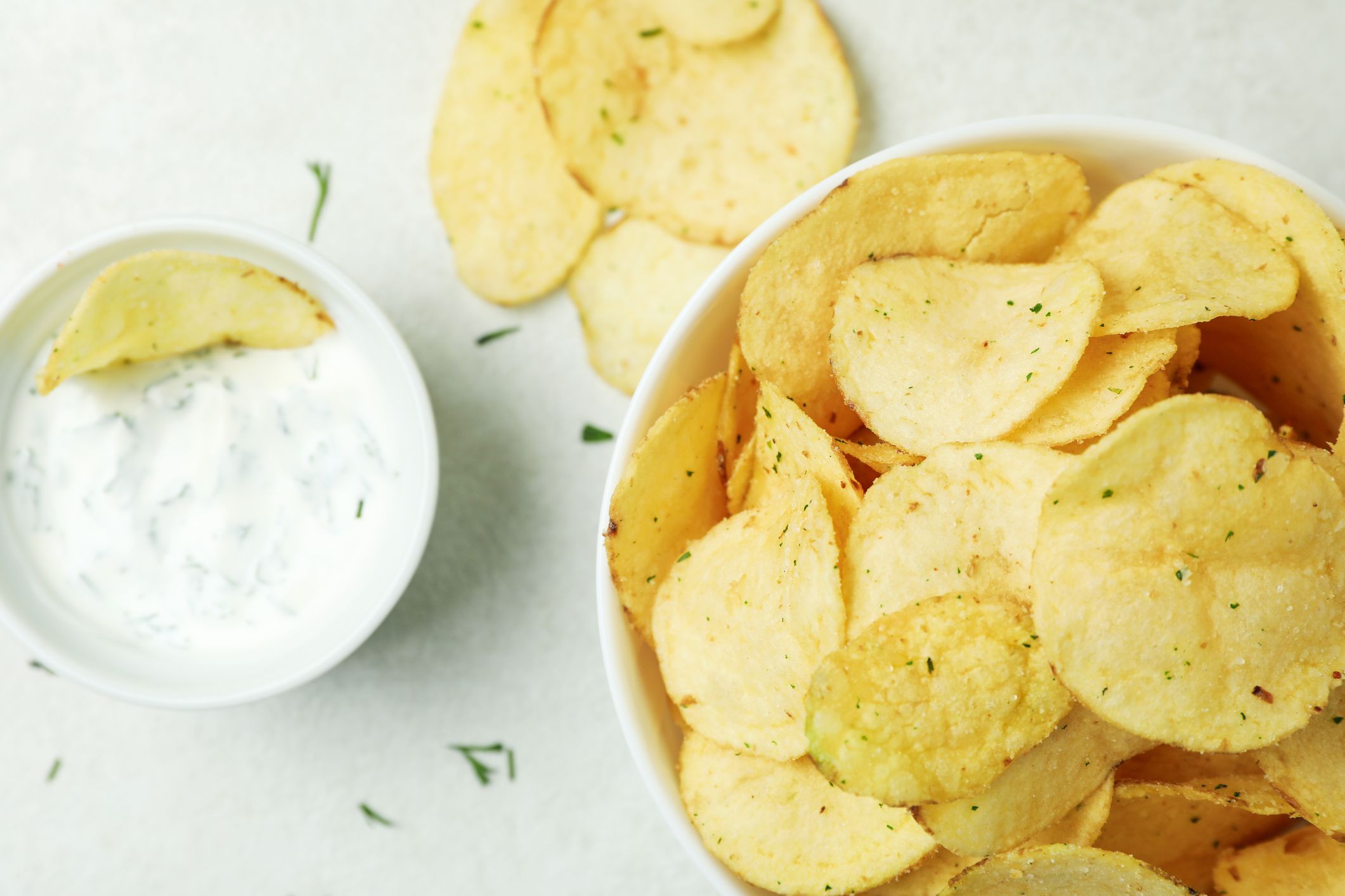 Tasty potato chips and sauce on white textured background