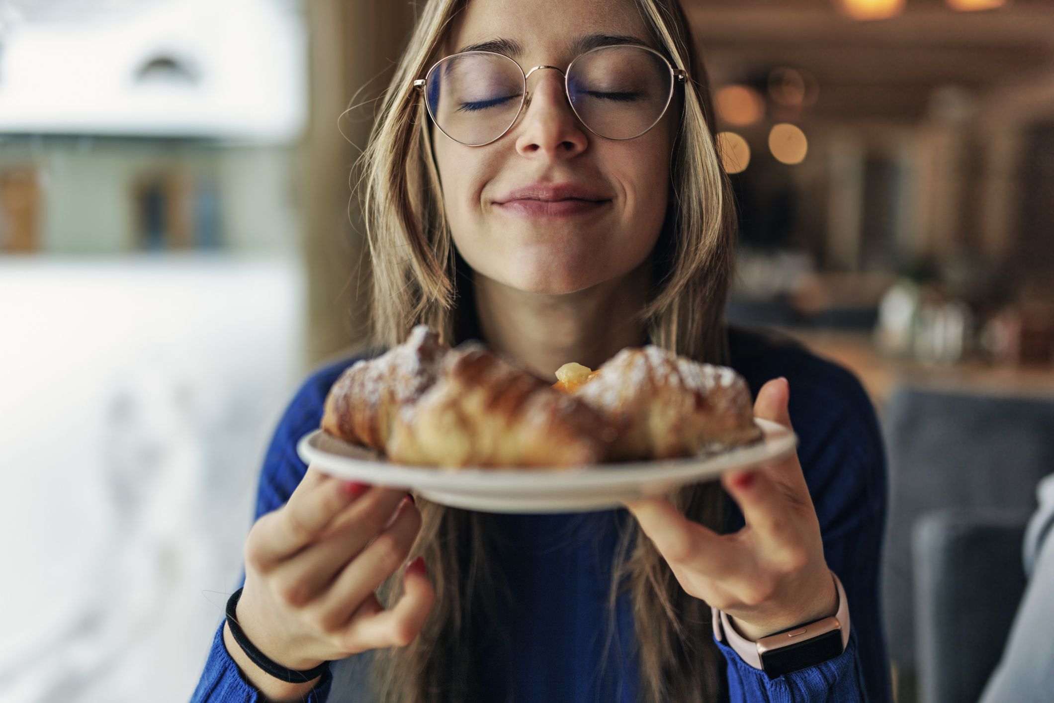 Teenage girl having breakfast in restaurant. She is smelling fresh, warm croissants.Canon R5