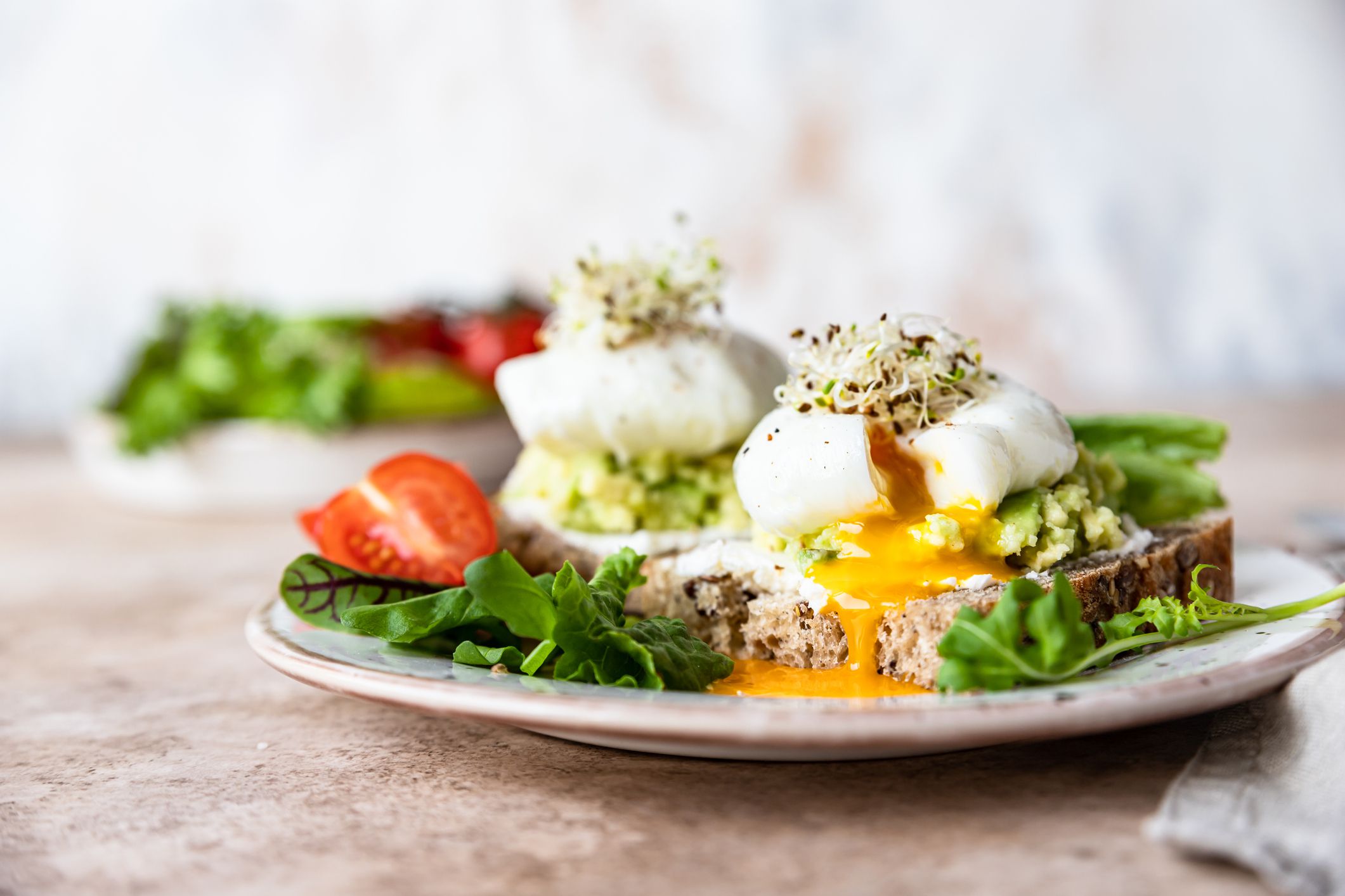 Sourdough bread with cream cheese, mashed avocado and poached egg served with salad leaves, tomatoes and sprouts on concrete background. Healthy breakfast or brunch. Diet food concept.