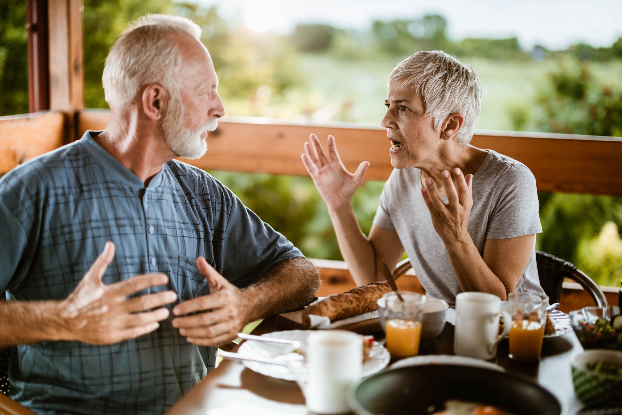 Frustrated senior couple arguing while having problems during breakfast on a balcony.