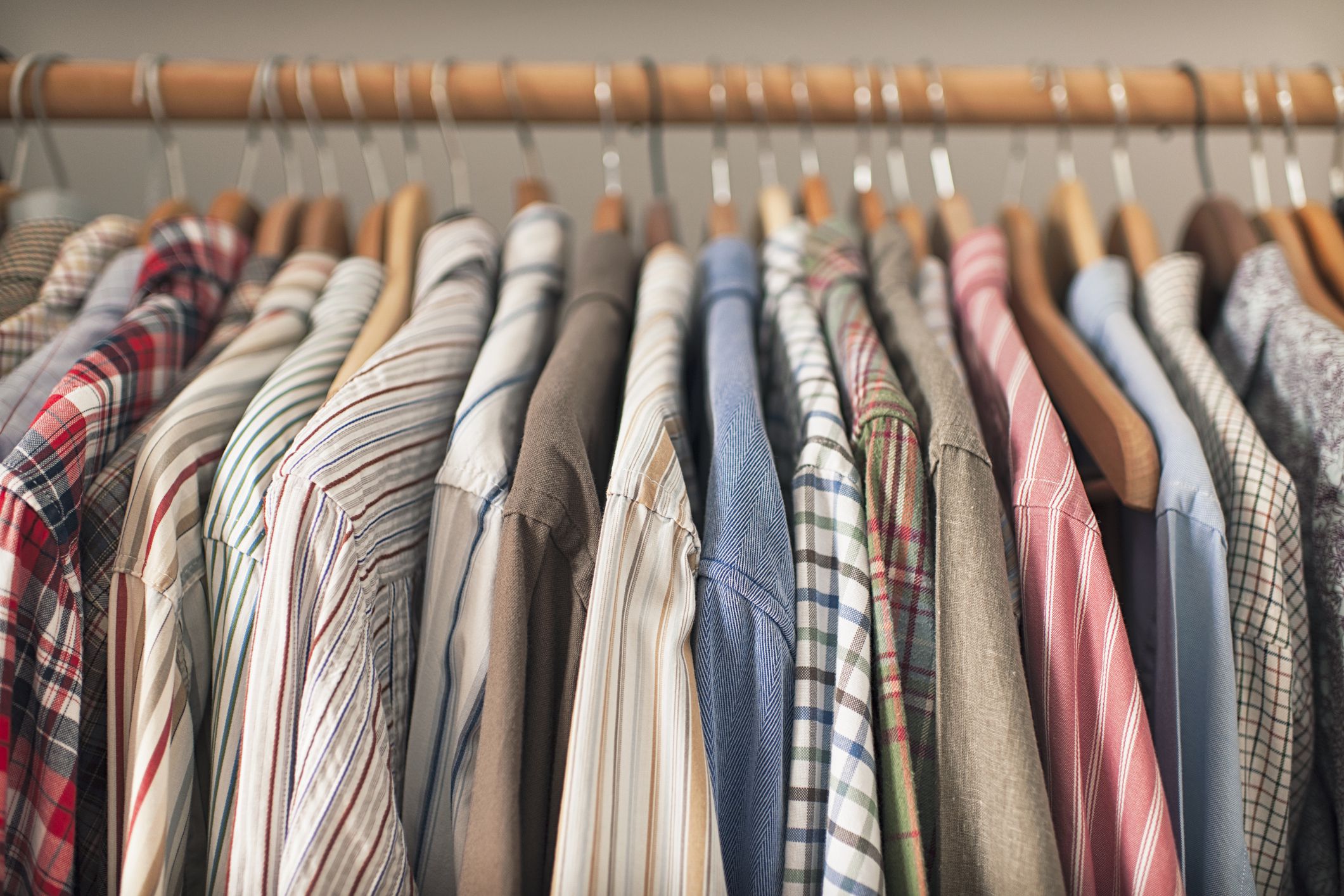 A variety of shirts hanging on a wooden clothes rack.