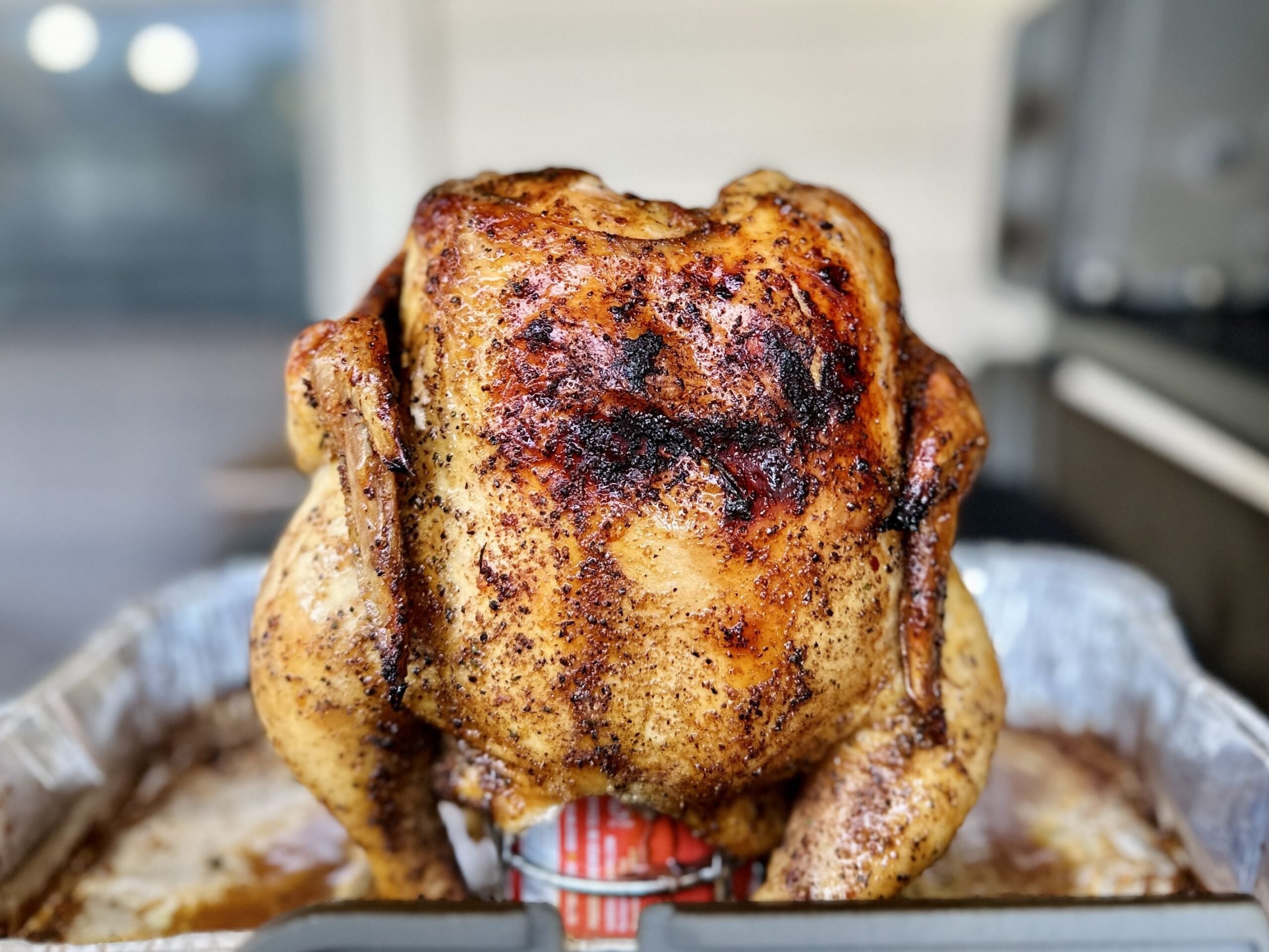 A beer can chicken, seasoned with spices and flavored by the beer inside of the can, is perched on a beer can chicken stand shortly after coming off a backyard barbecue grill.