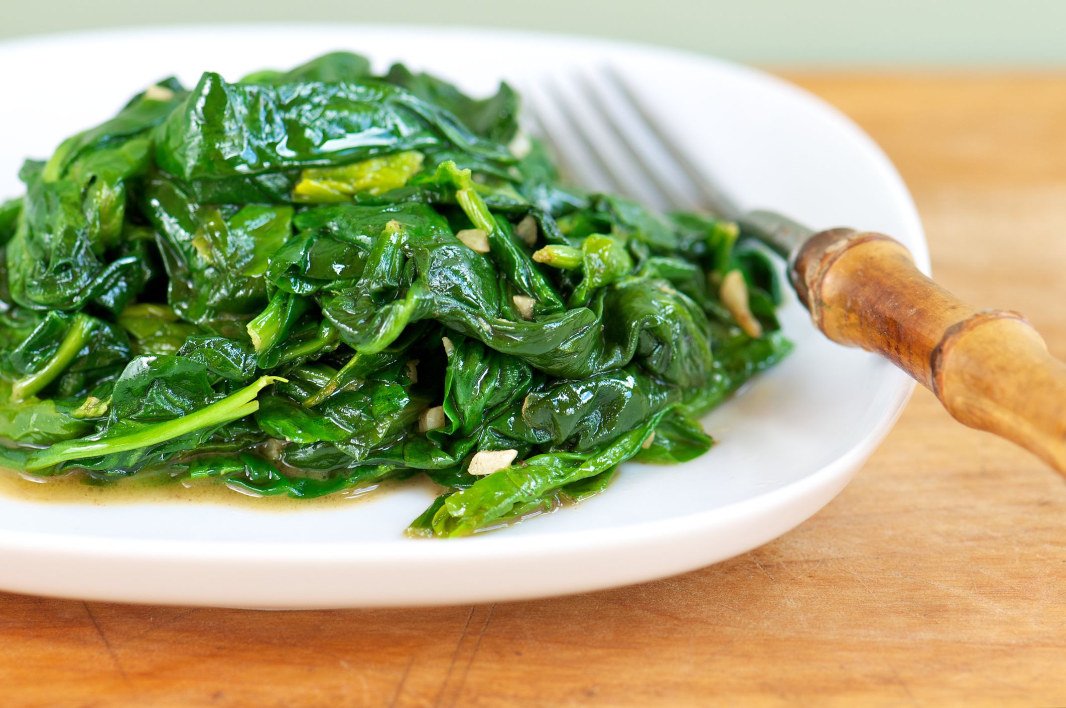 White plate of fresh sauteed spinach with garlic with fork on wood