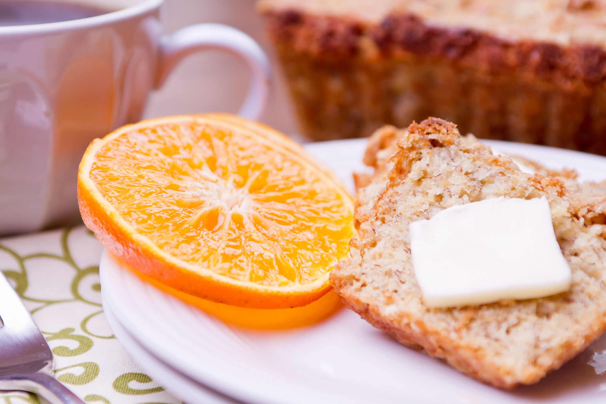 Delicious banana bread with orange slices. Shown with green and white linens and fork. Coffee mug in background.Shallow depth of field.