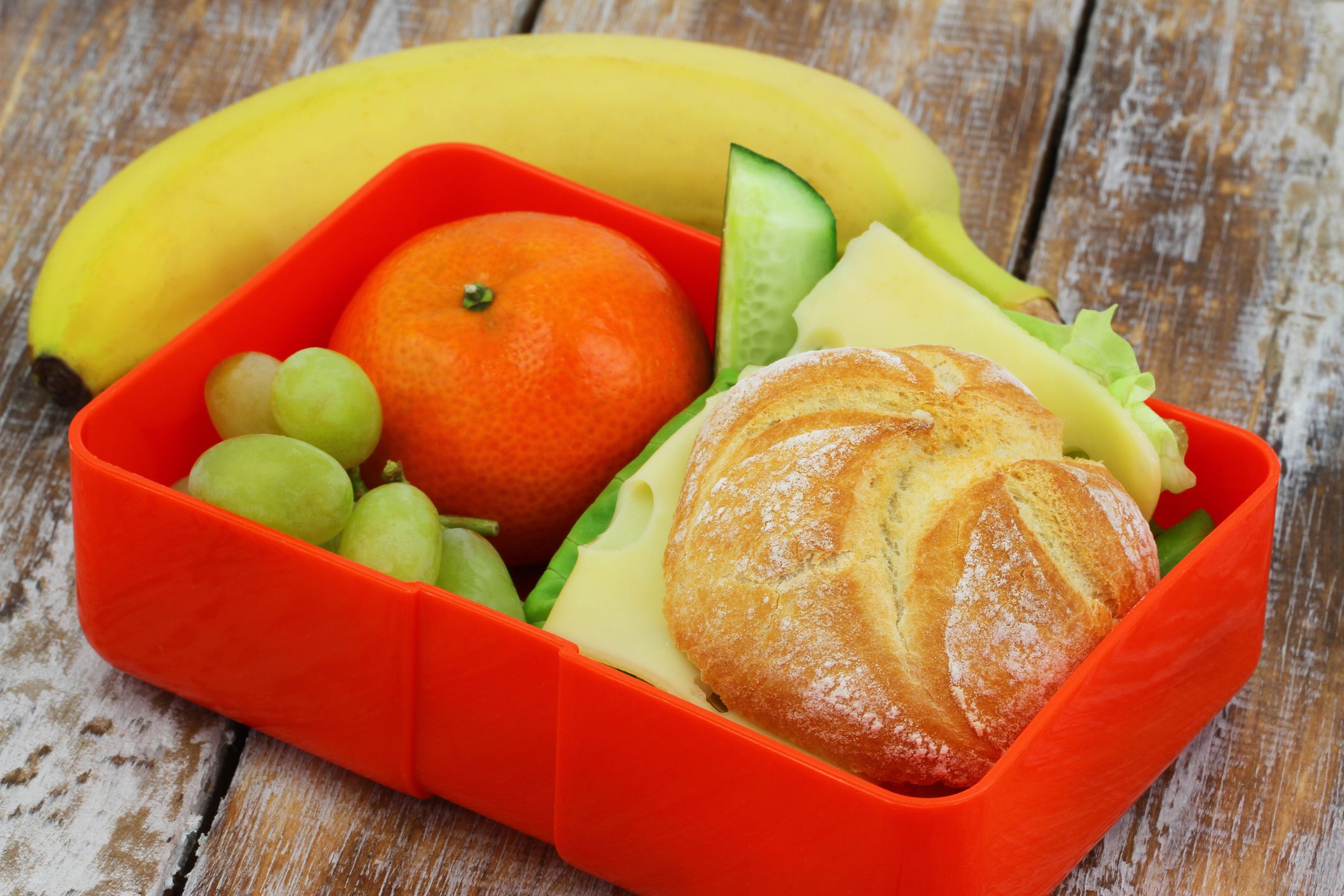 Lunch box containing cheese sandwich, mandarine, grapes and banana