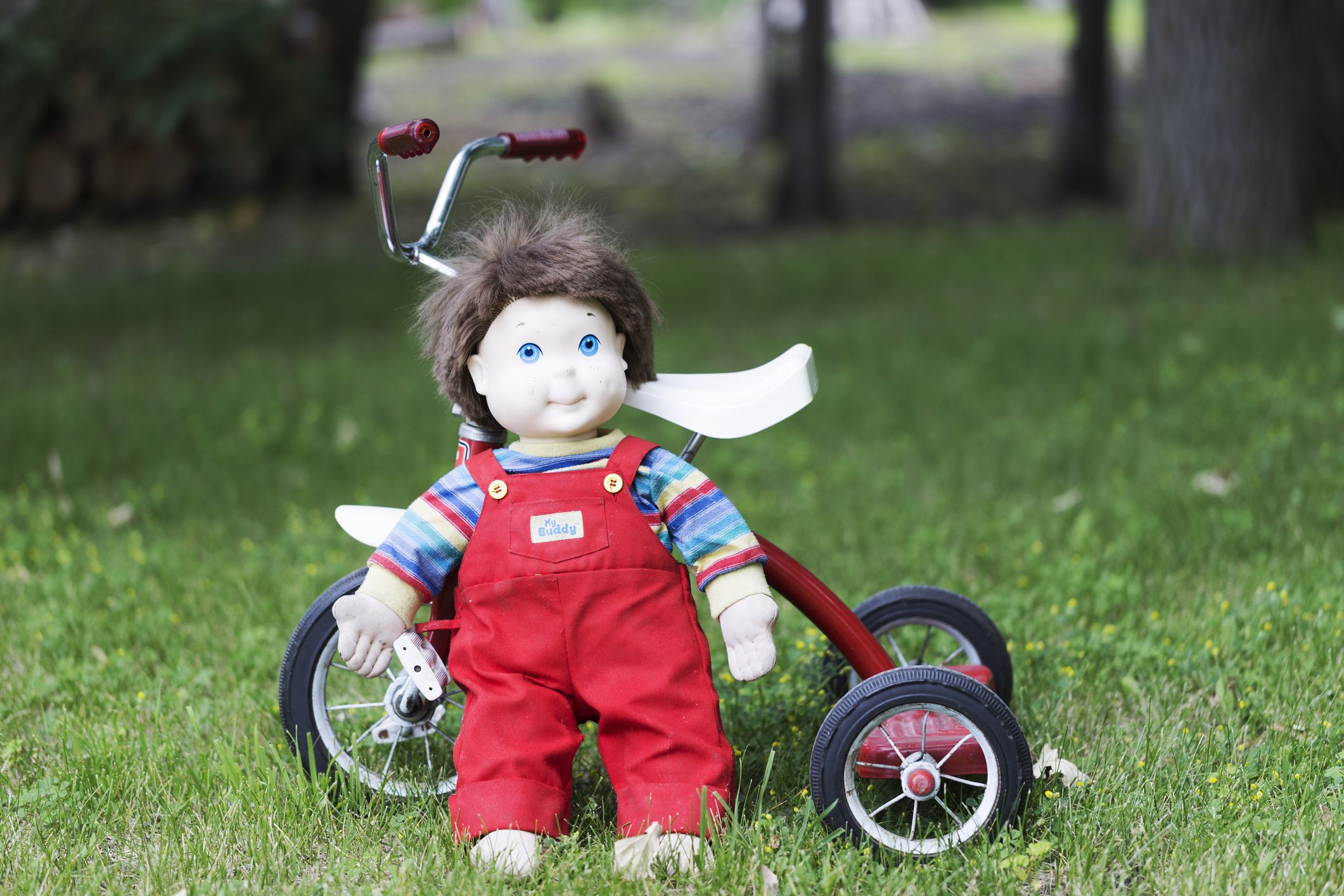 Fosston, USA - June 25, 2016: A vintage My Buddy doll is standing in front of an old tricycle. Made by Hasbro in 1985, the My Buddy boy doll was intended to appeal to little boys and teach them about caring for their friends.
