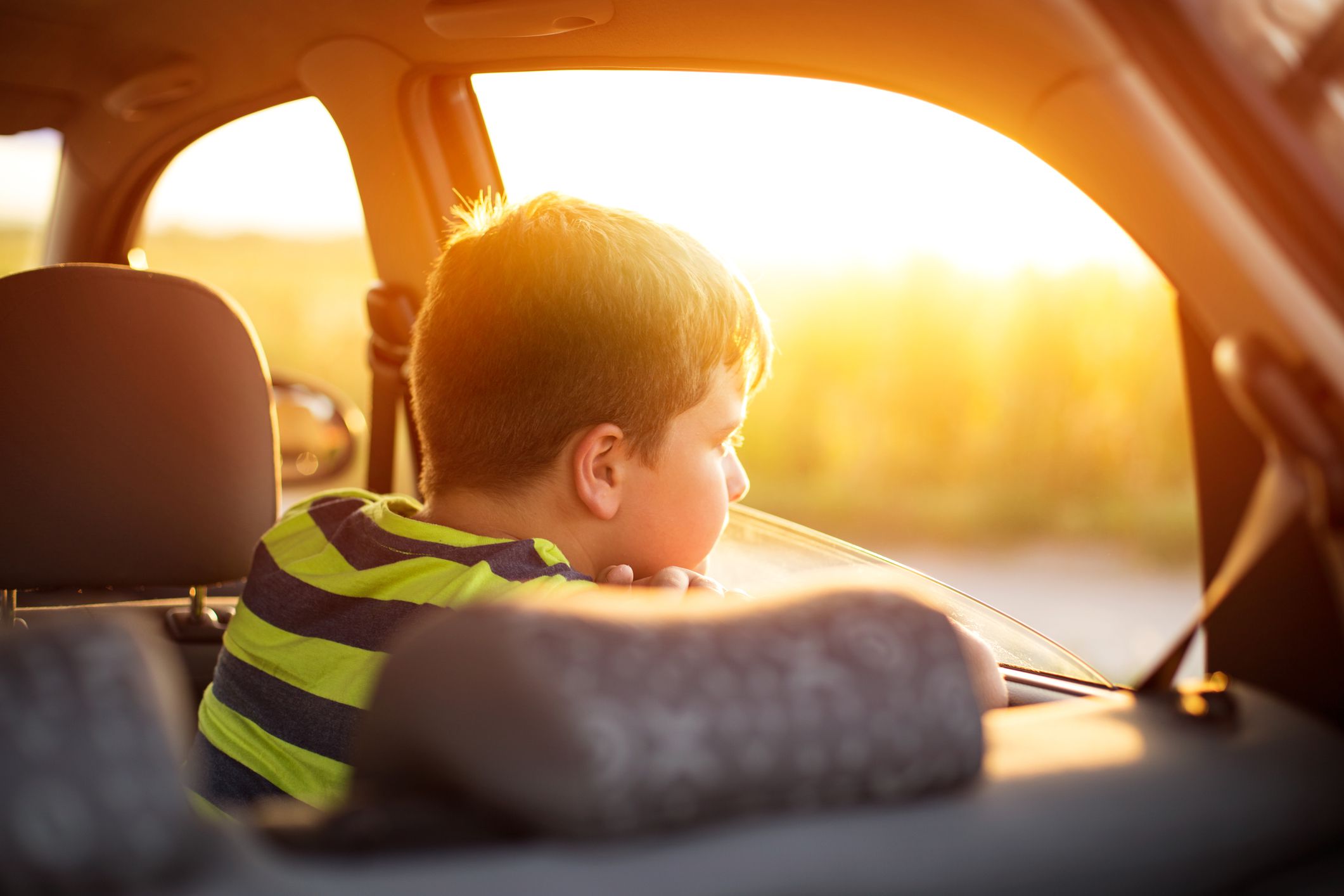 Boy on back seat of a car looking at camera in sunset
