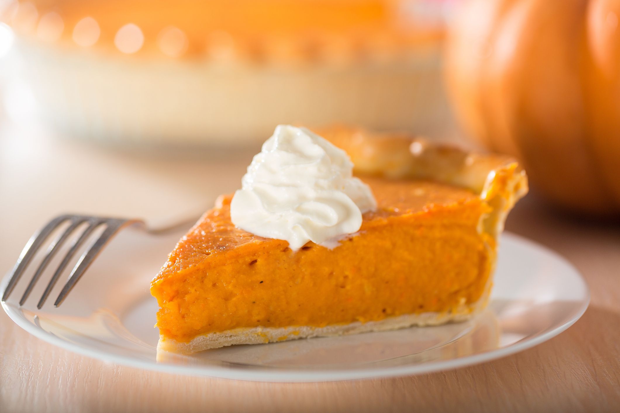 Pumpkin pie with swirls of whipped cream on decorative plate. Whole pie in soft focus in background. Macro with shallow dof