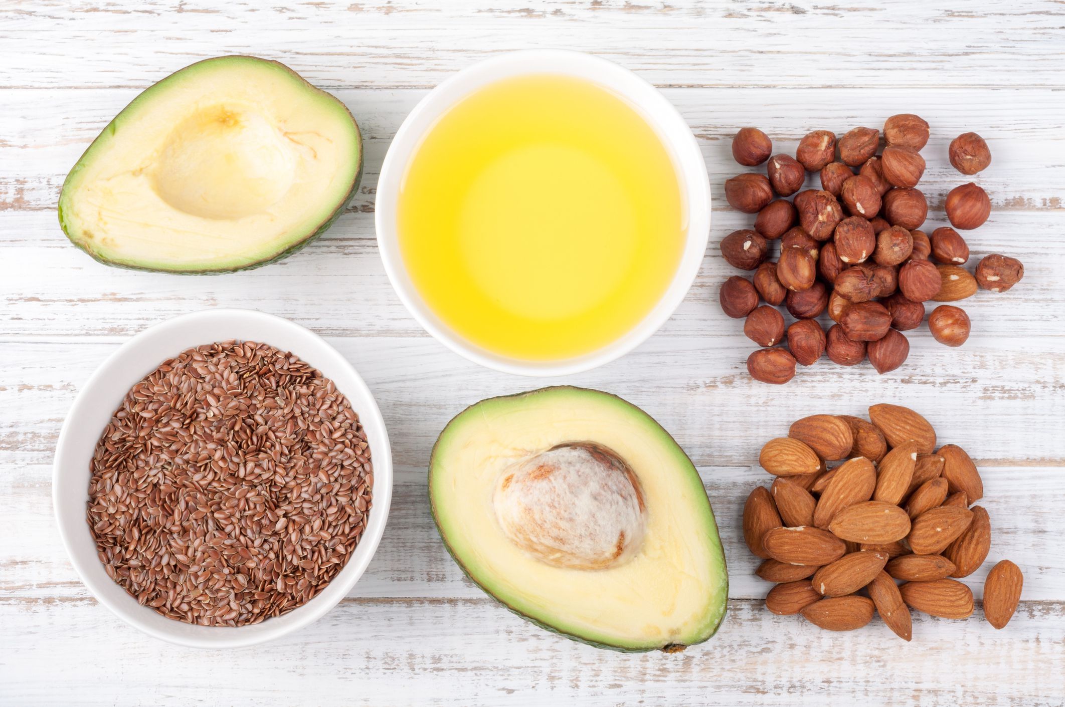Foods with healthy fats. Sources of omega 3 - avocado, olive oil, nuts and flax seed on wooden background. Healthy food concept. Top view