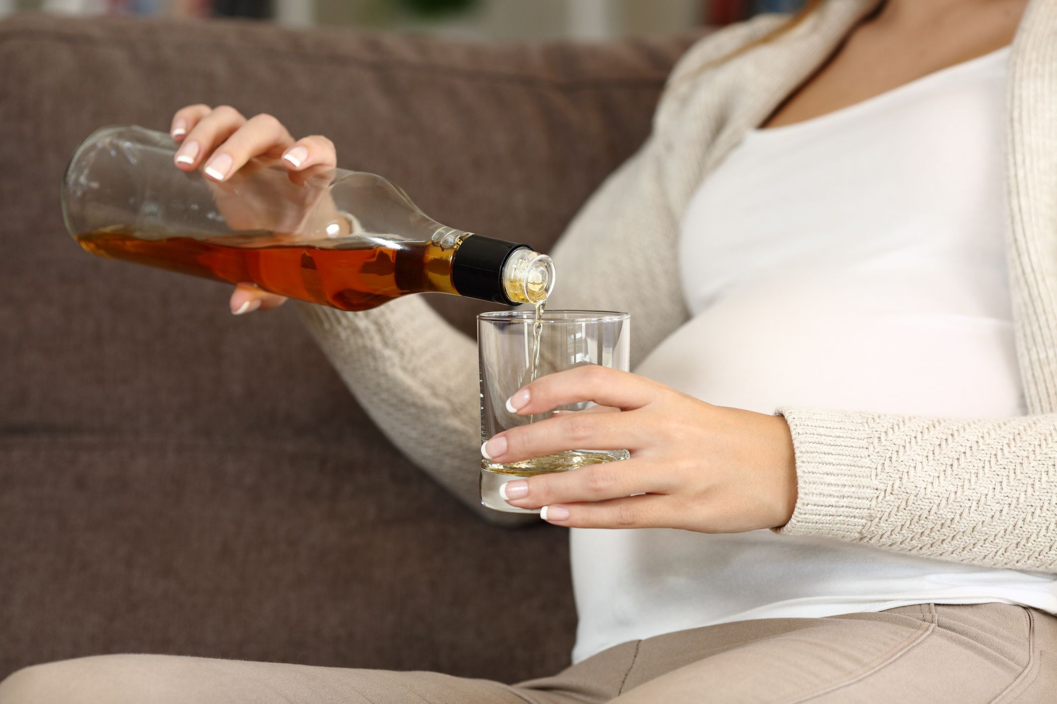 Close up of an irresponsible pregnant woman drinking alcohol sitting on a couch at home