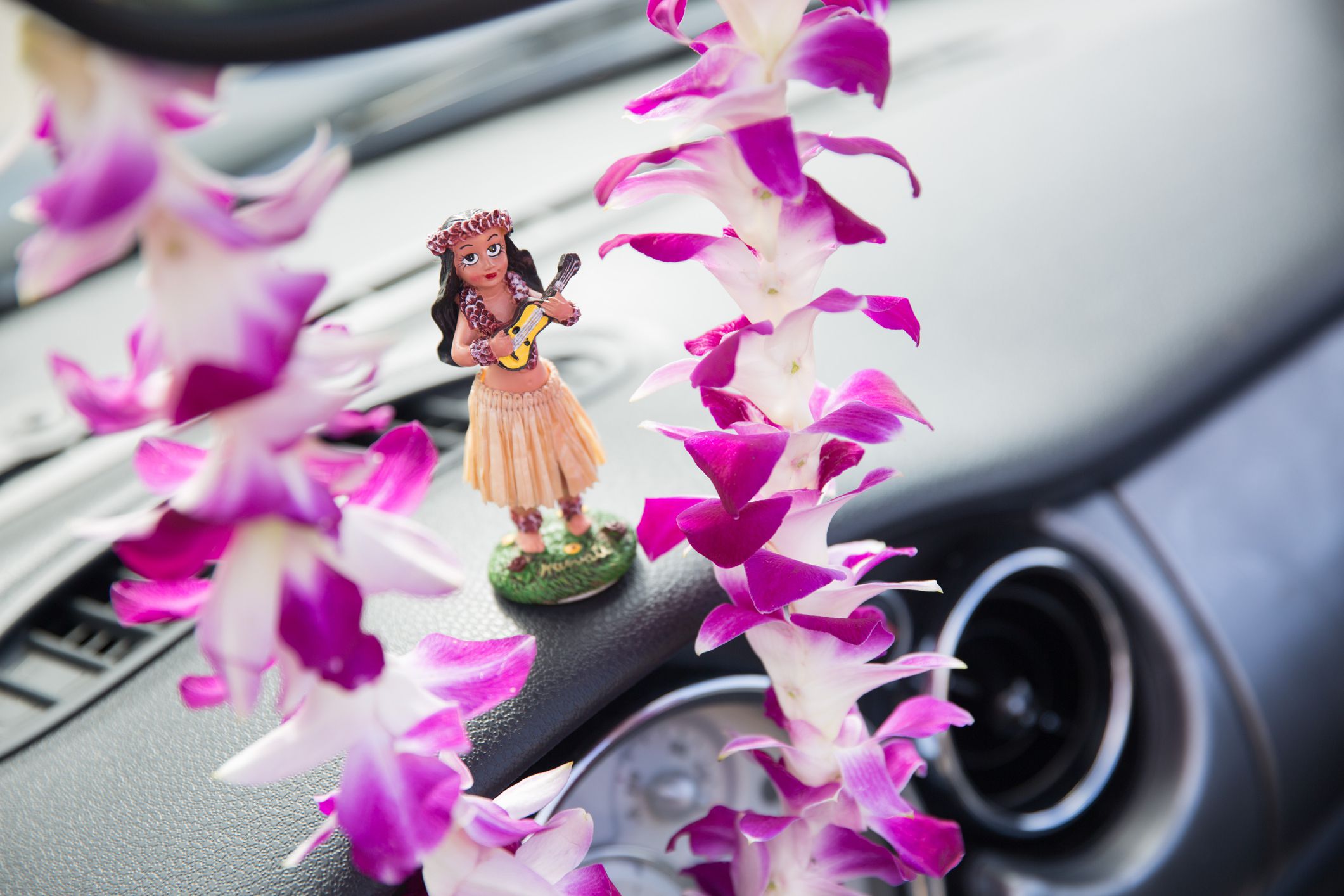 Hawaii road trip - car hula dancer doll dancing on the dashboard and Hawaiian Orchid Le Tourism and travel freedom concept.