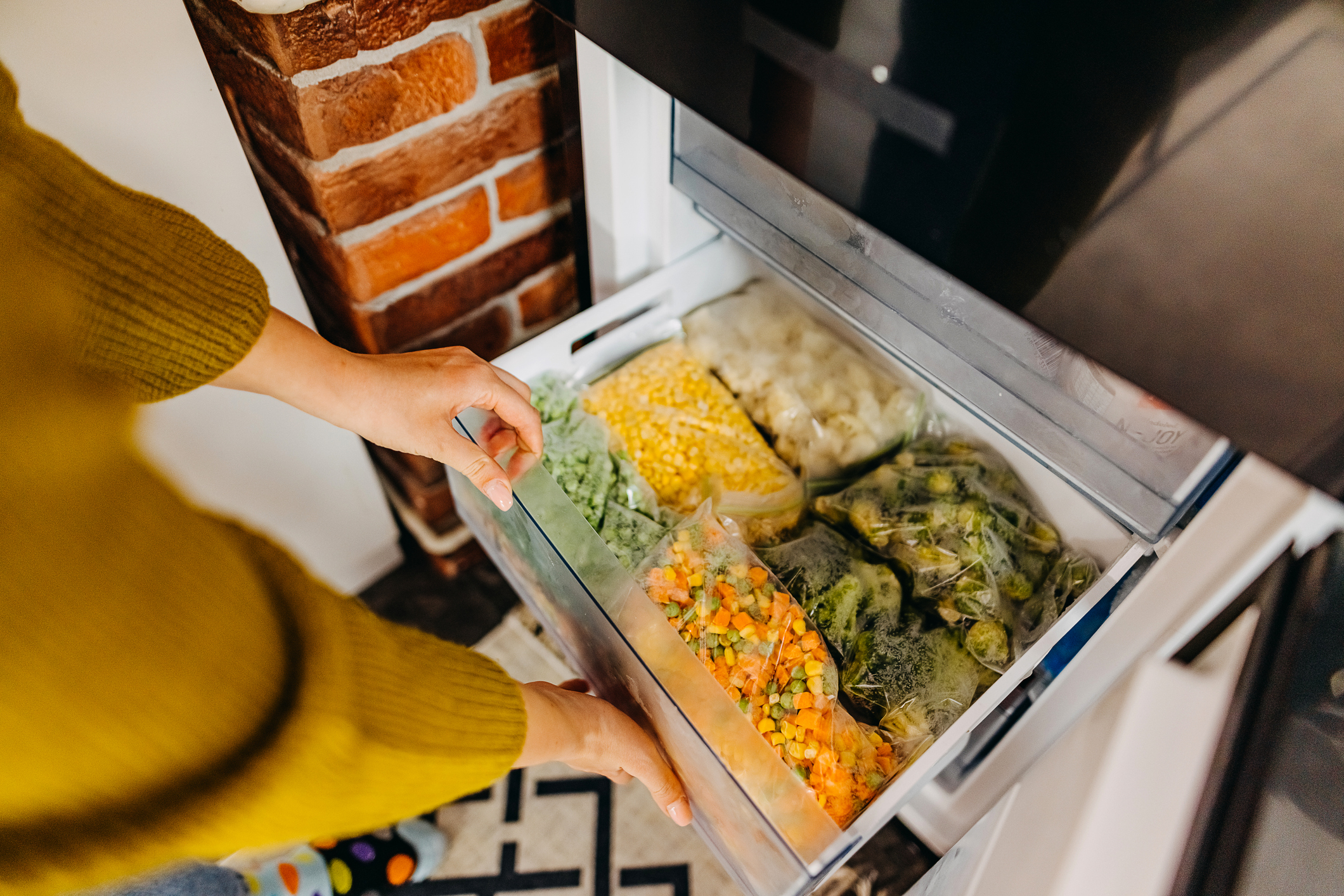 Woman Opening Freezer Slide Door Filled With Bags of Vegetables, Very Organized, Selective Focus