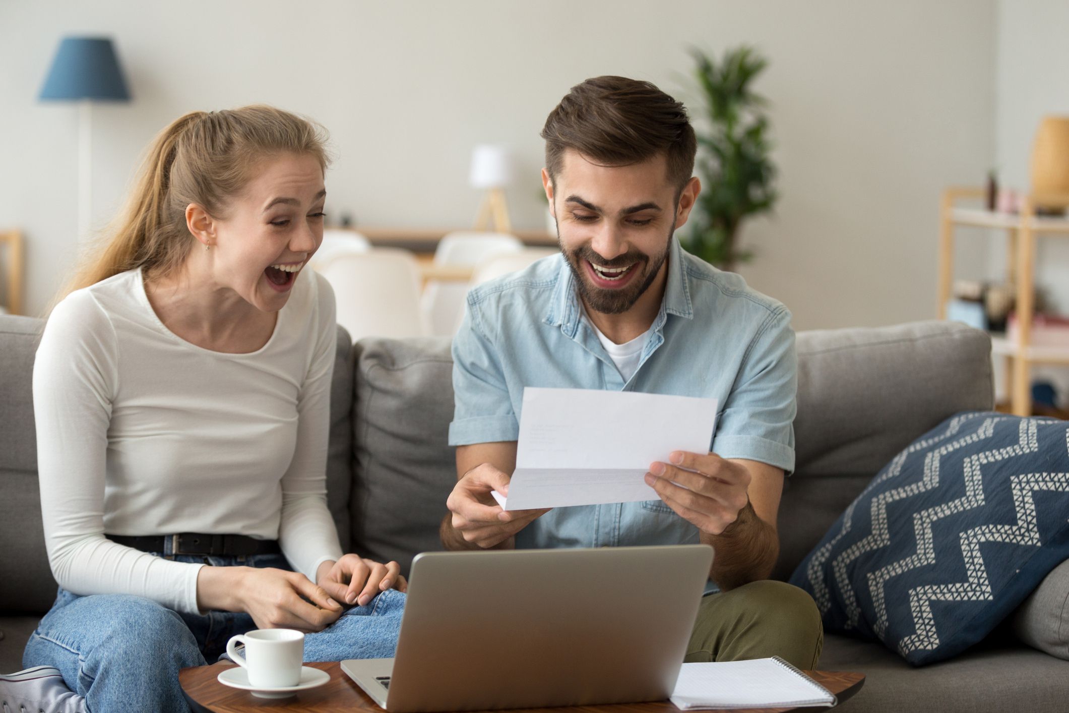 Excited amazed happy couple winners screaming with joy rejoicing reading good news holding mail paper letter celebrating taxes refund, cheap great offer, economy promotion in bank statement at home