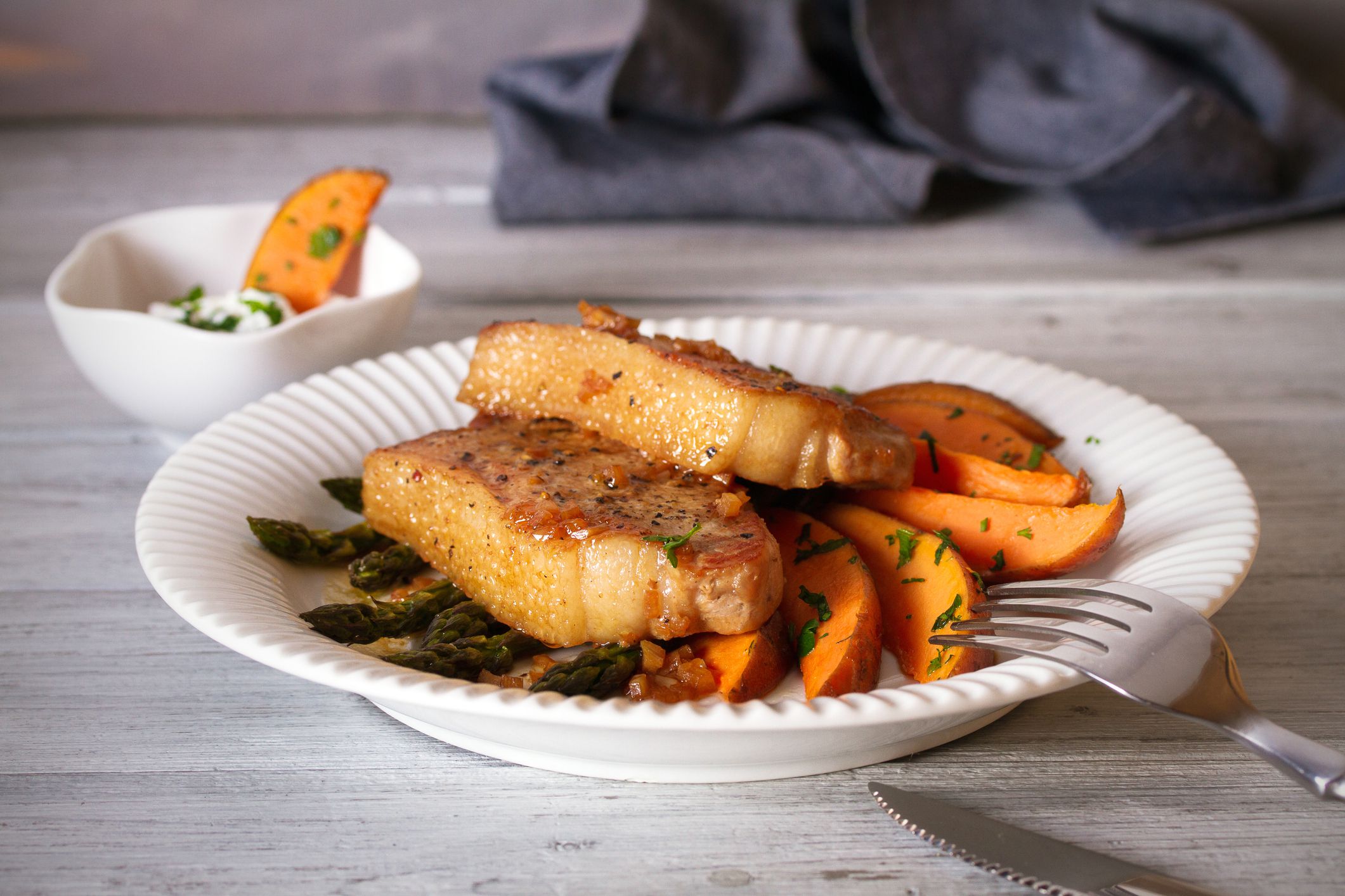 Juicy broiled pork chop steaks with asparagus, sweet potatoes and yogurt sauce. horizontal image