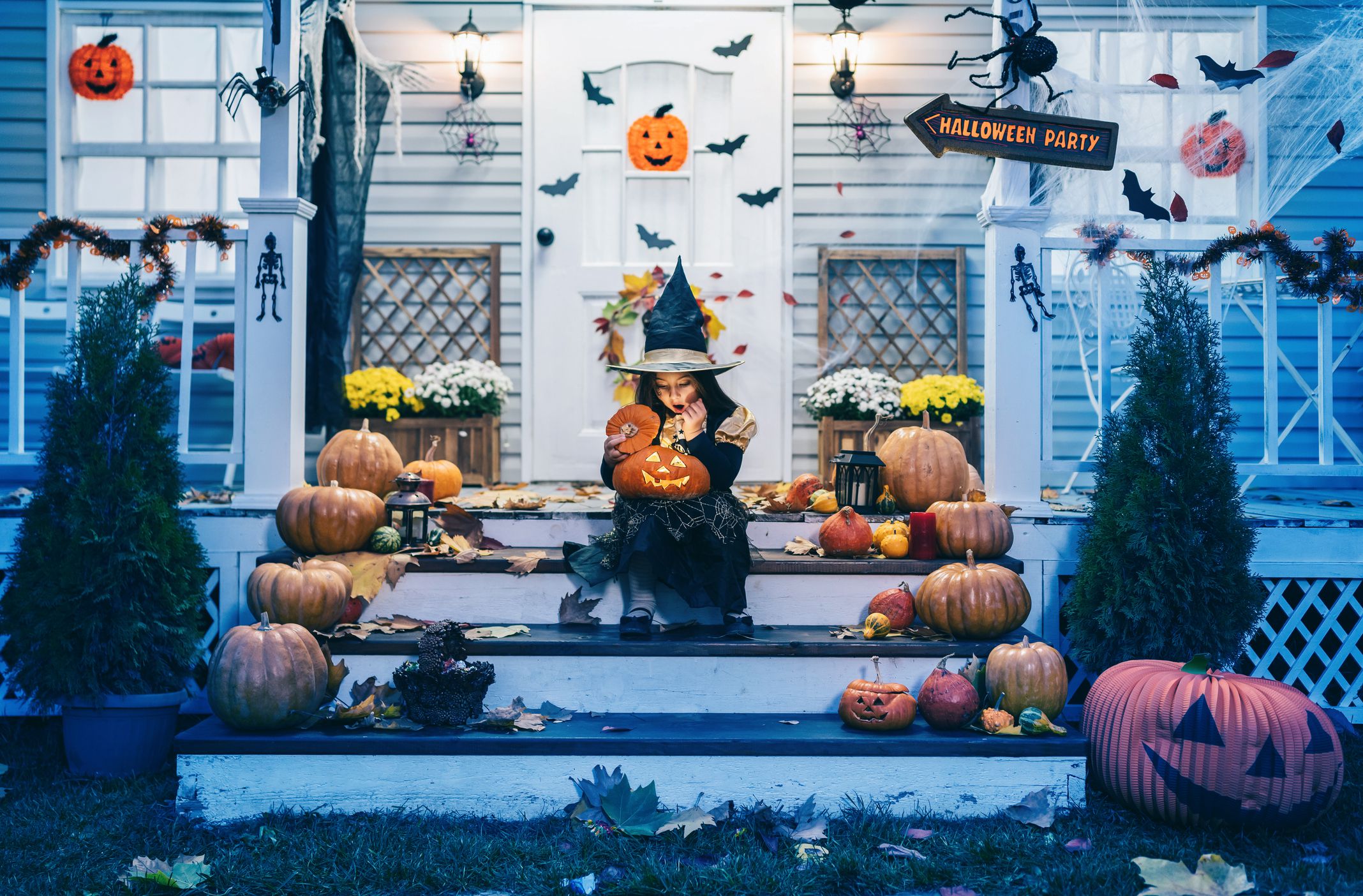 Little girl in witch costume sitting on the stairs in front of the house and holding Jack-o-Lantern Pumpkins on Halloween trick or treat