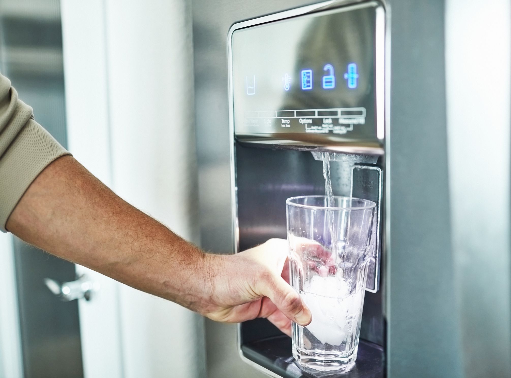 Unrecognizable man filling glass from refrigerator water dispenser