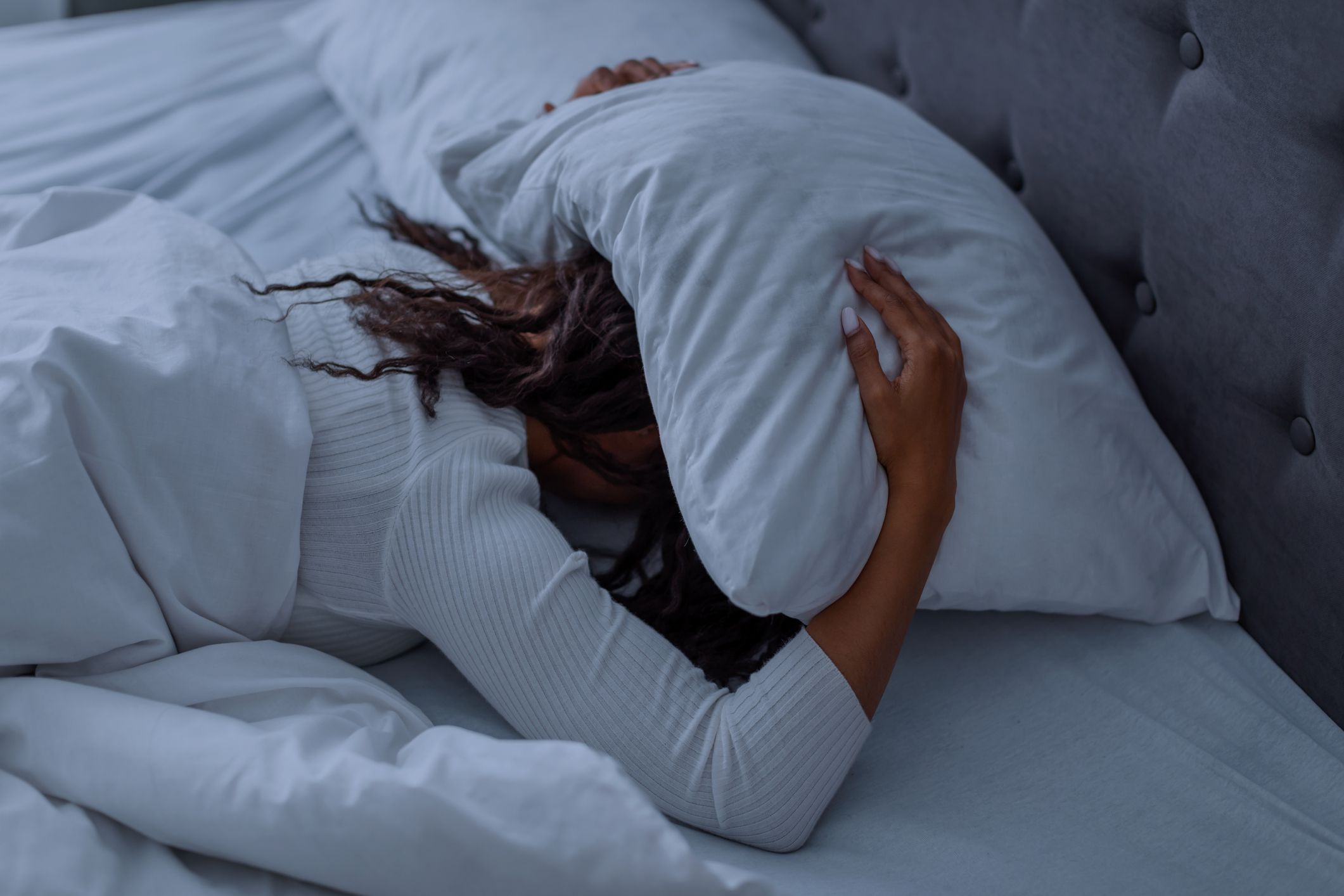 Sleeping Problem. Stressed African American lady lying alone in bed covering head under pillow feeling afraid or depressed, suffering from insomnia or mental problems after breakup