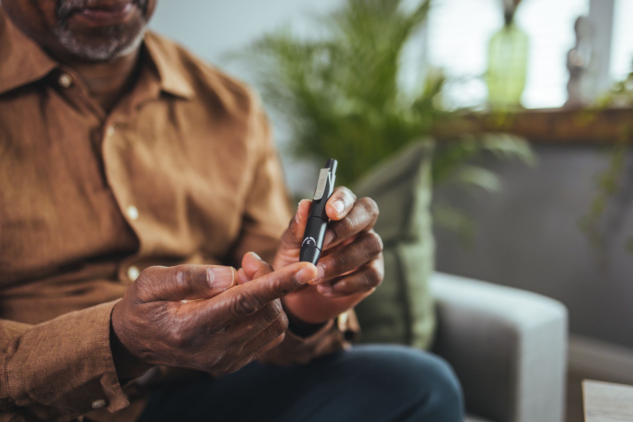 A modern African man sits at a table in the living room and takes blood from his finger due to diabetes. Everyday life of a man of African American nationality with a chronic disease who uses a glucose tester.