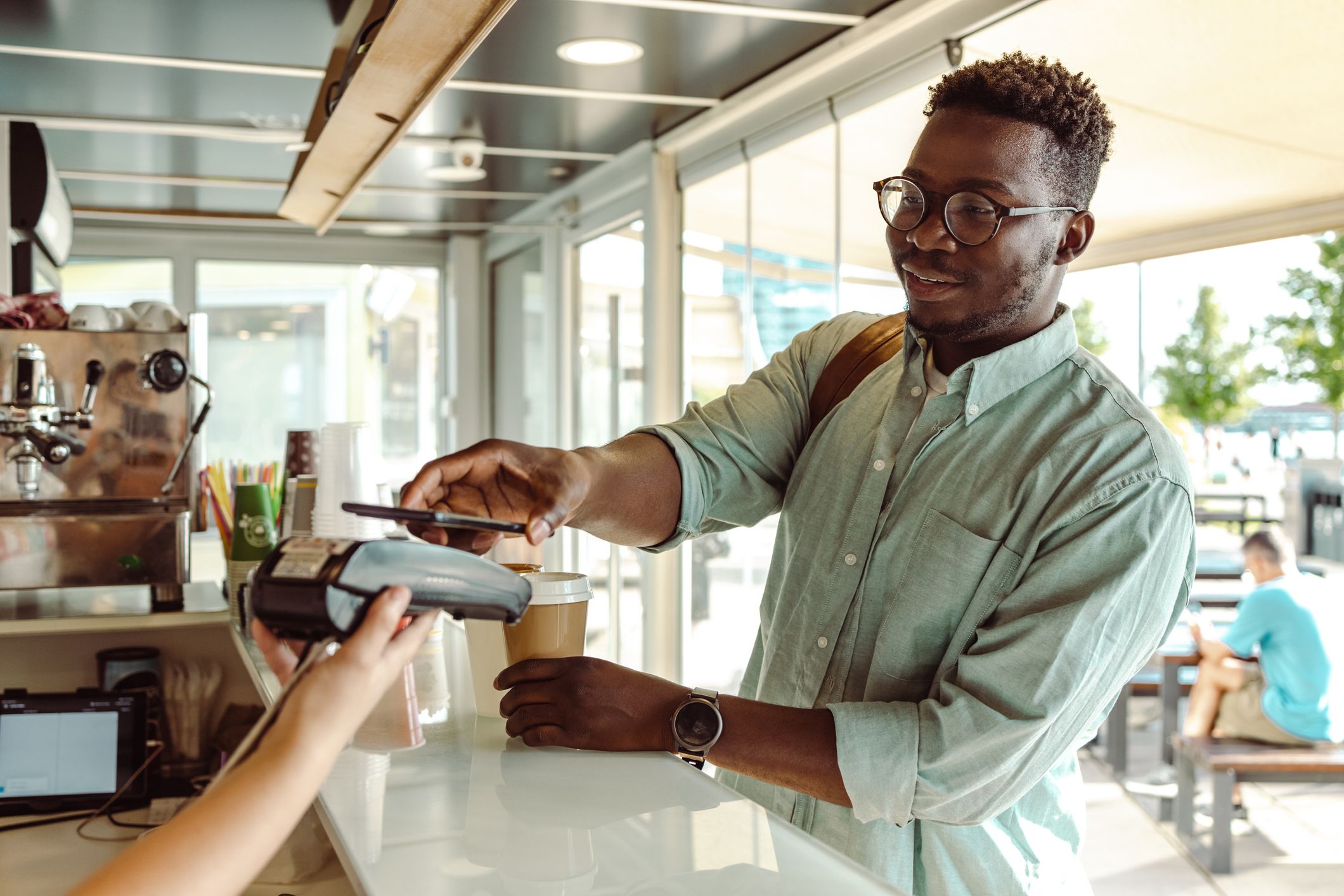 Young African American student paying a coffee with his phone