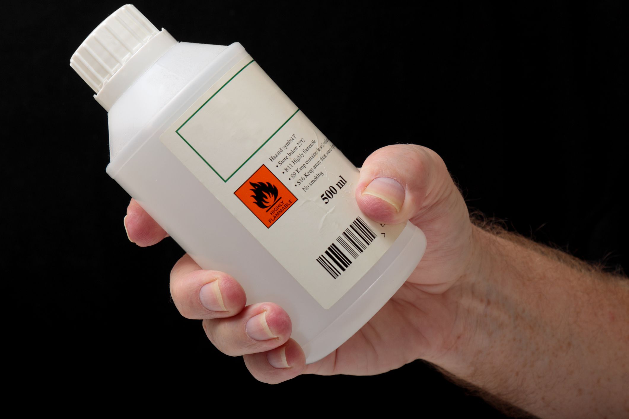 a male hand holds a half litre plastic container of highly flammable liquid. Plain background - not isolated