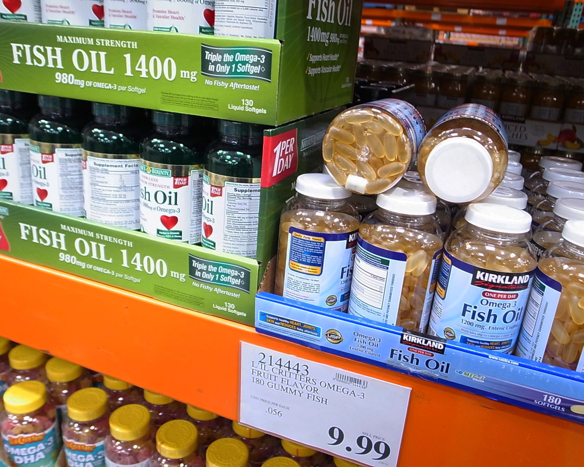 Bottles of Kirkland Signature Omega-3 Fish Oil gummies are displayed on a store shelf next to Maximum Strength Fish Oil capsules, with a price tag showing $9.99 for 180 gummies.