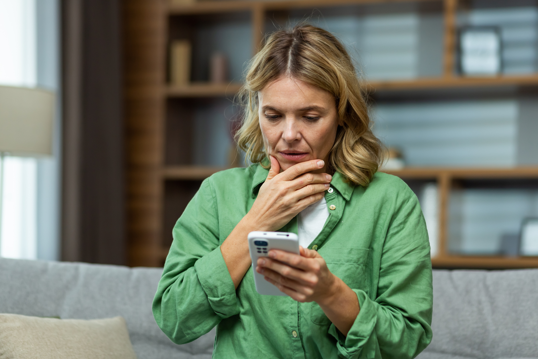 Woman Sitting on Couch at Home, Looking Down on Smartphone While Holding It, Reading