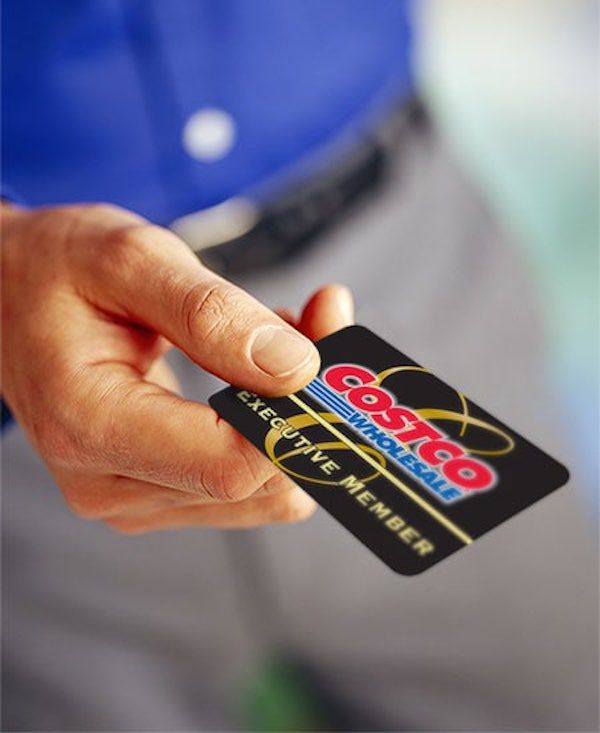 A person in a blue shirt holds a black Costco Wholesale Executive Member card between their thumb and fingers.