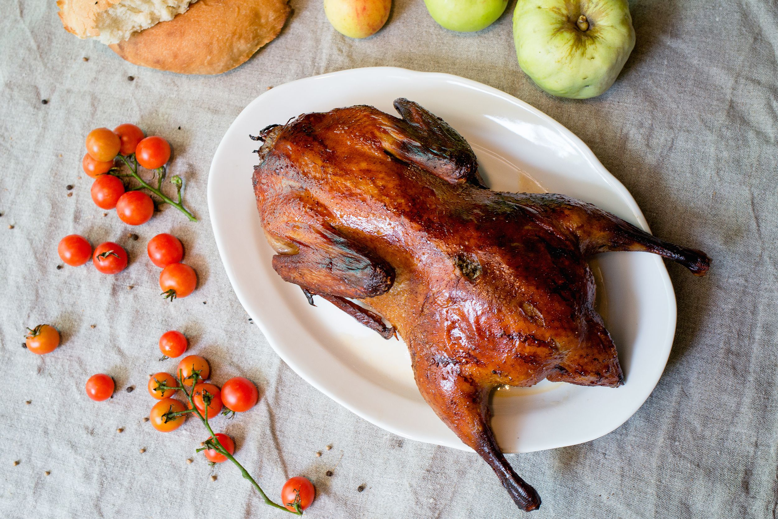 Top view of peking duck on a white plate on a light grey tablecloth with mini tomatoes and fruits
