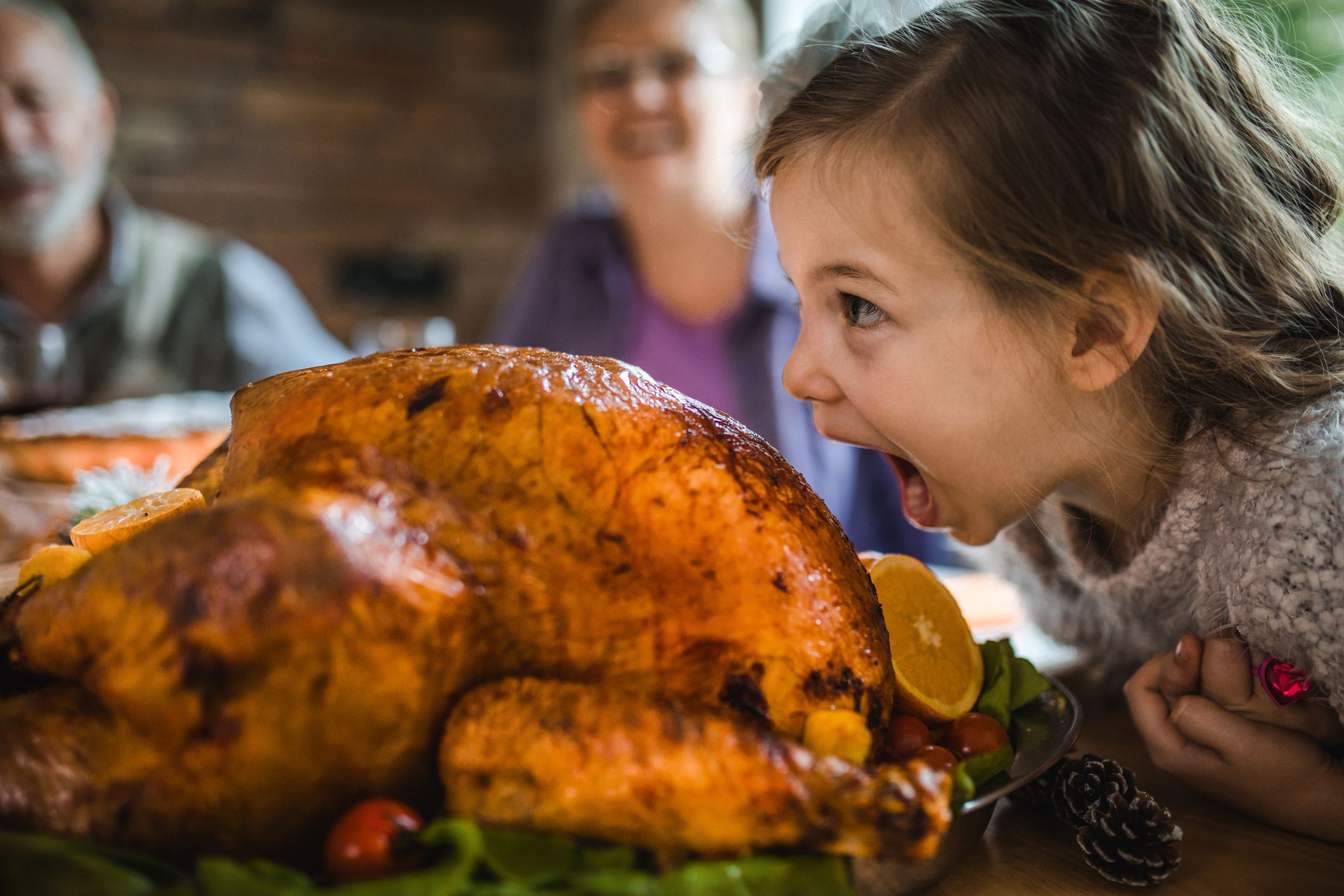 Cute little girl having fun while about to bite a stuffed turkey during Thanksgiving dinner in dining room.