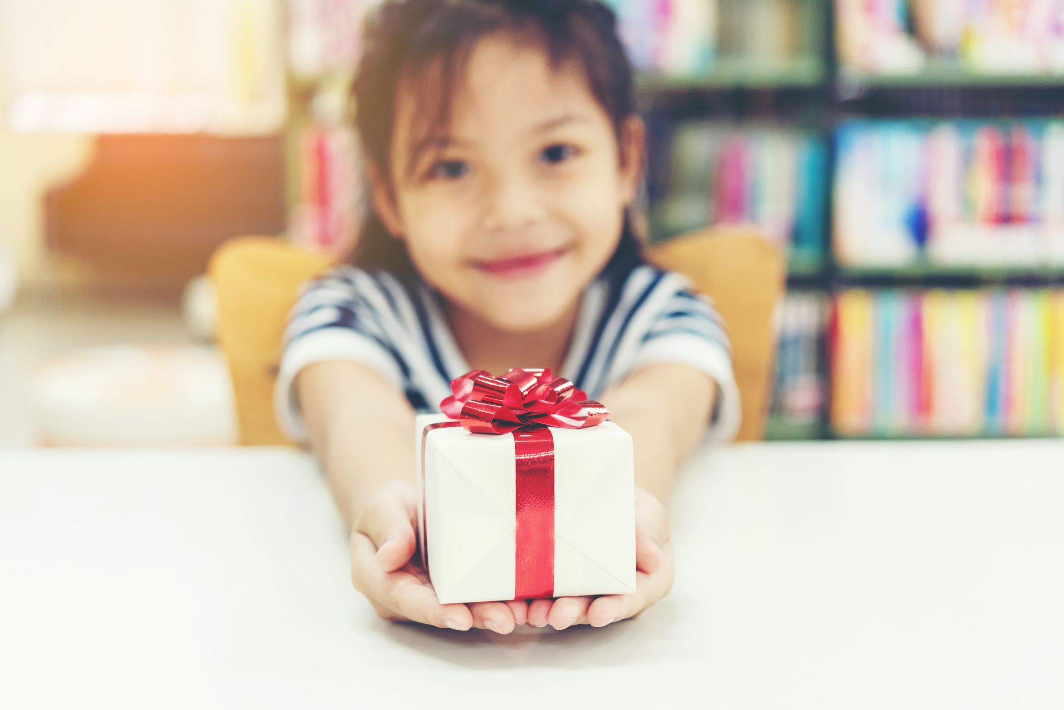 Gift box for kids girl. White box with red bow in the girl hands for give a gift in the library