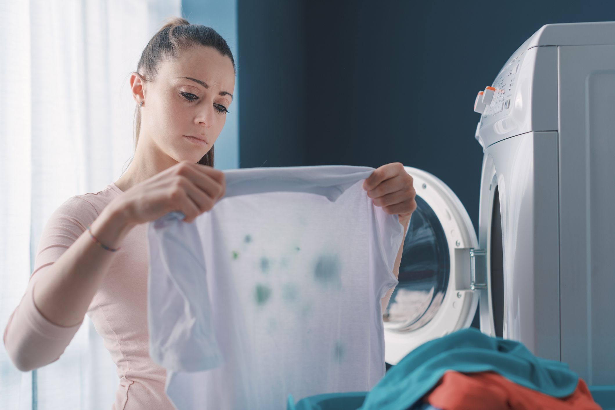 Disappointed woman standing next to the washing machine and holding stained clothes