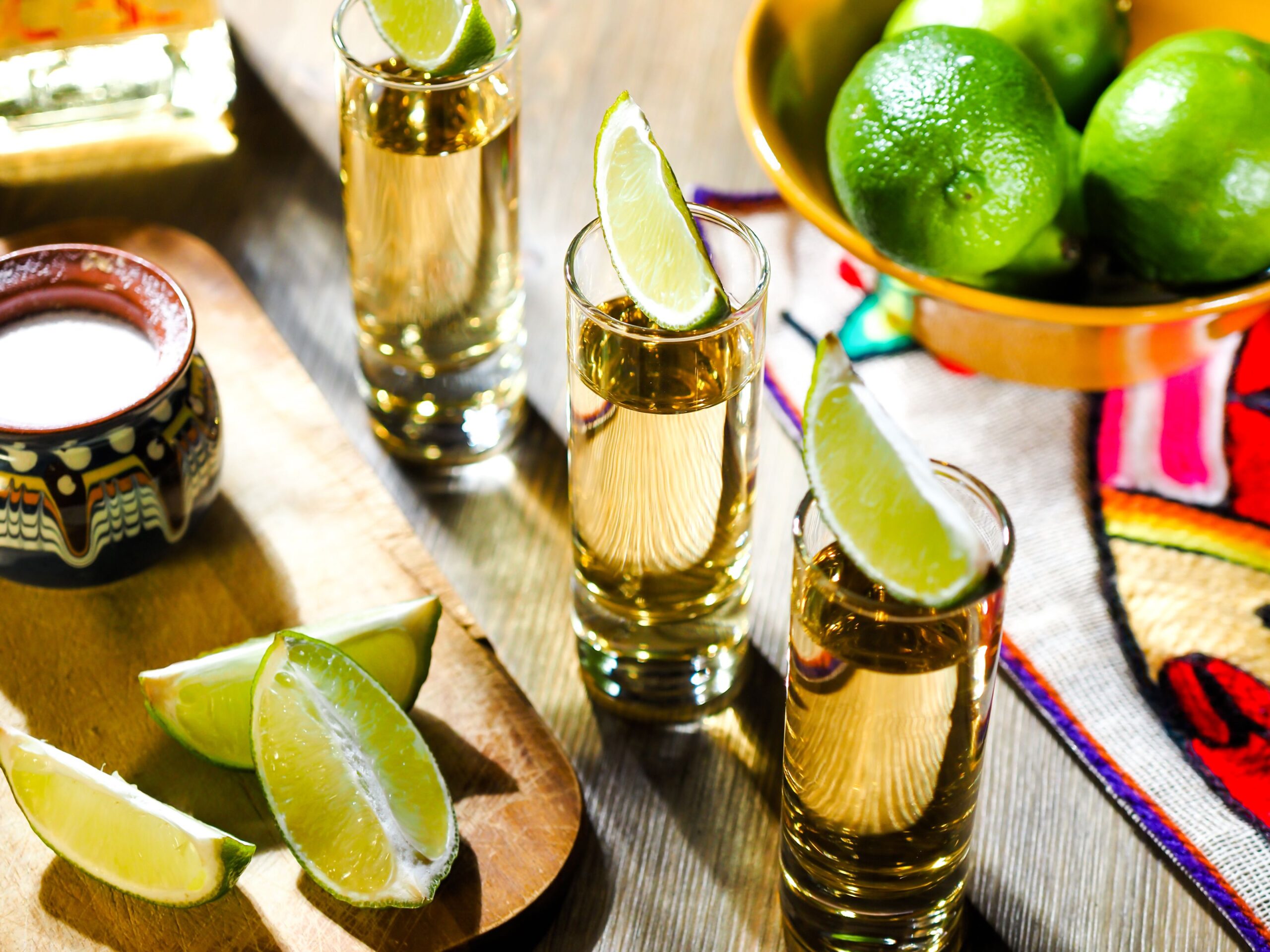 Three shots of tequila in tall shot glasses with lime wedges on top