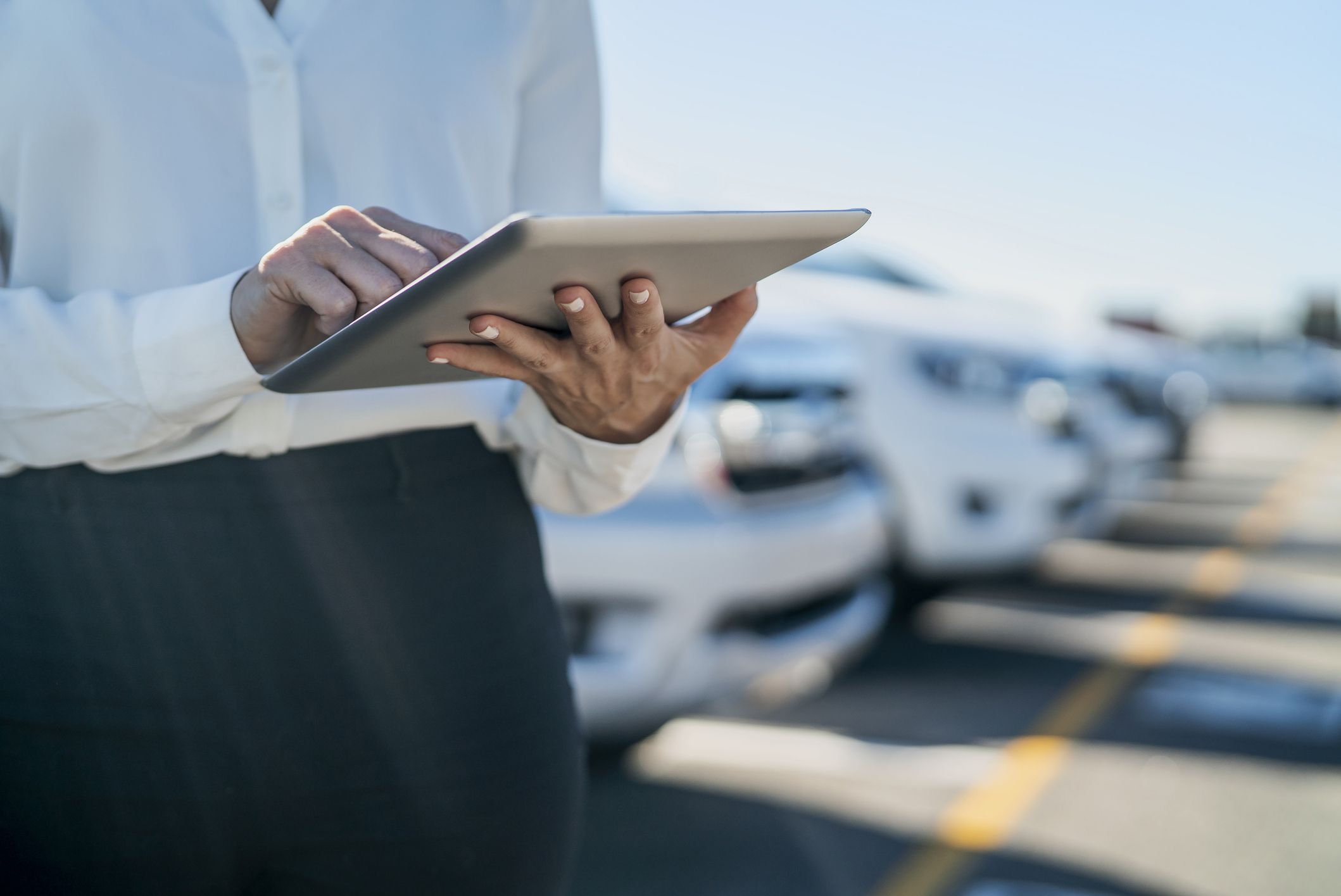 Midsection of car saleswoman using digital tablet at dealership parking lot during daytime