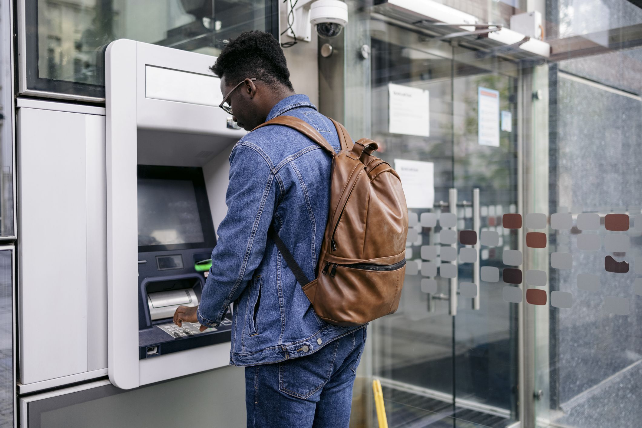 Handsome young man stopping by an ATM in the city and using a credit card to retrieve cash from his bank account