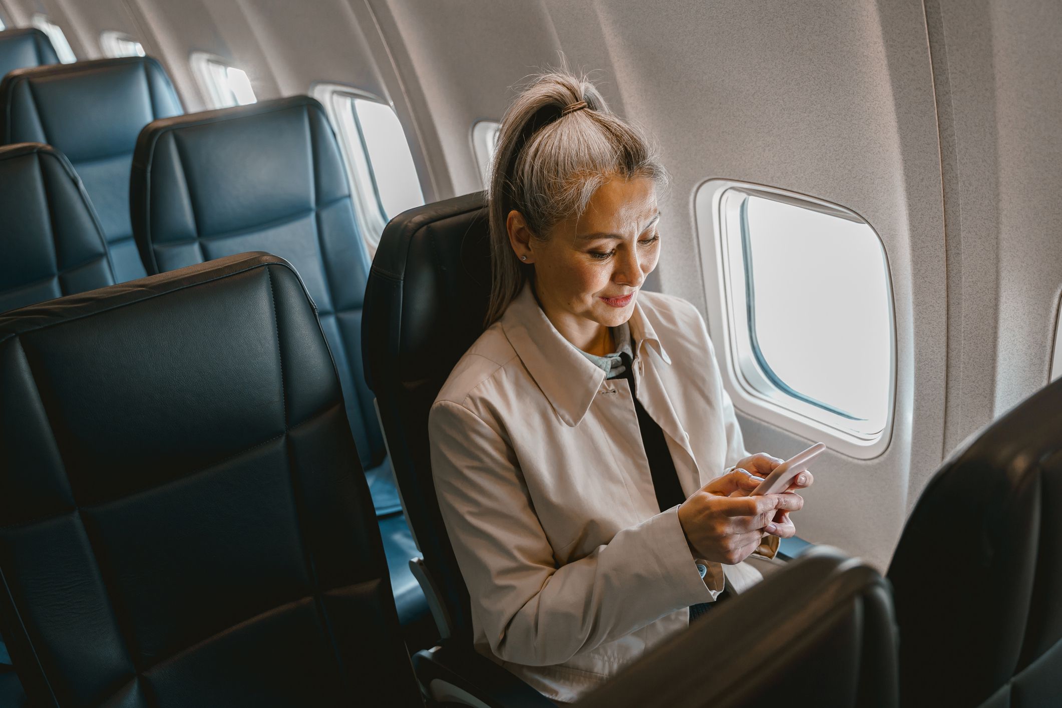 Asian woman passenger sitting in the airplane and use phone during boarding. High quality photo