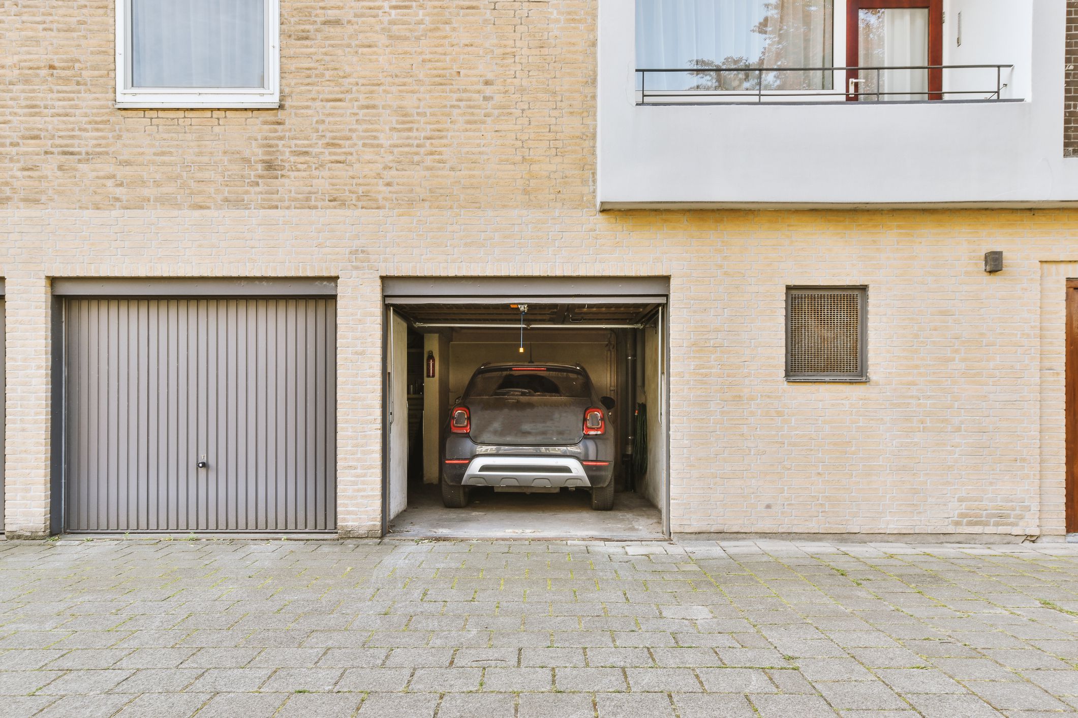 Narrow garage with car and opened door and brick walls in modern building at daytime