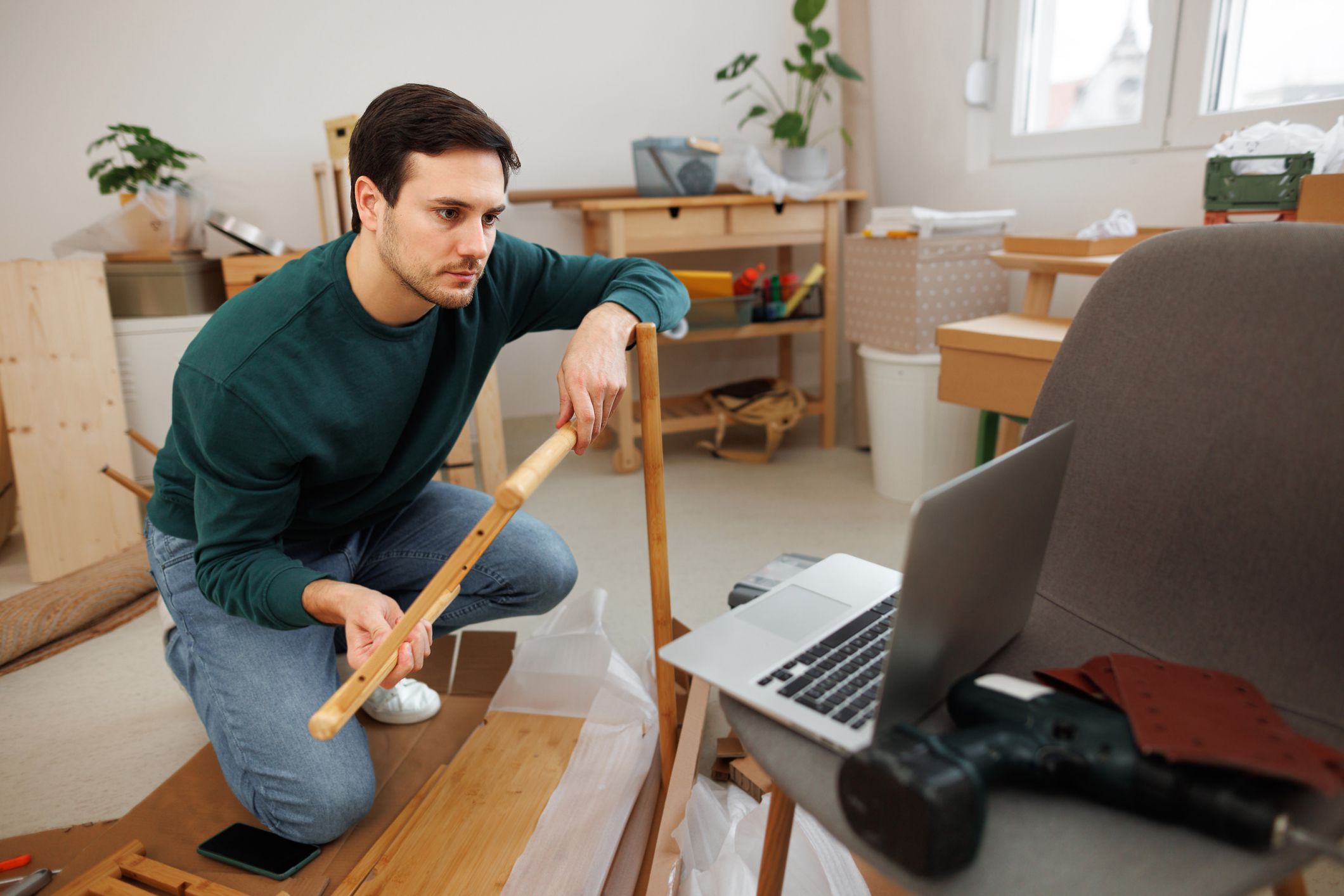 Young man watching tutorial how to assembly shelf on a laptop at his new apartment