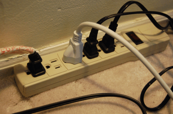 A power strip plugged into a wall outlet, with several white and black power cords connected to it.