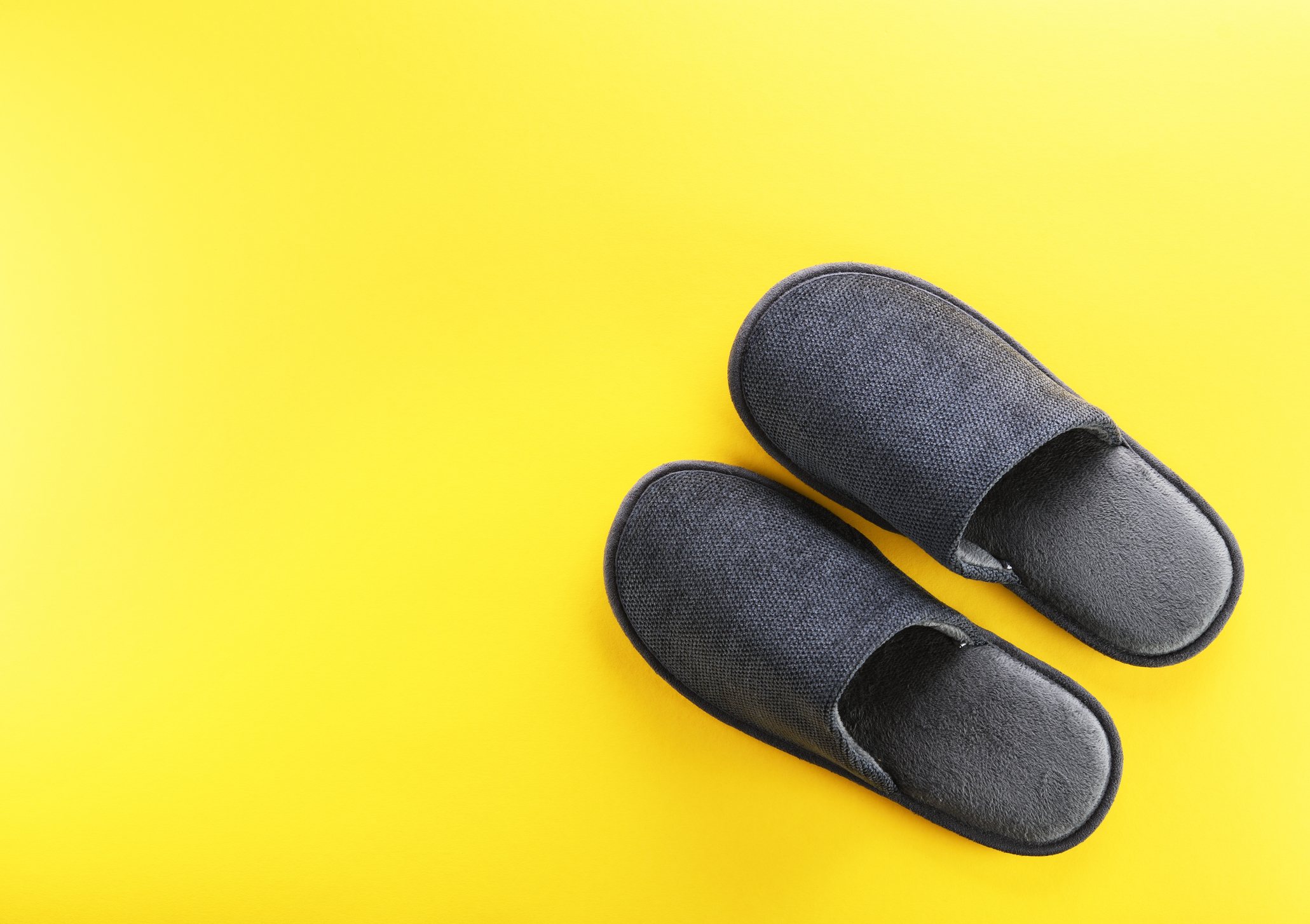 A pair of dark grey male slippers on the mid to bottom right, on a light yellow background