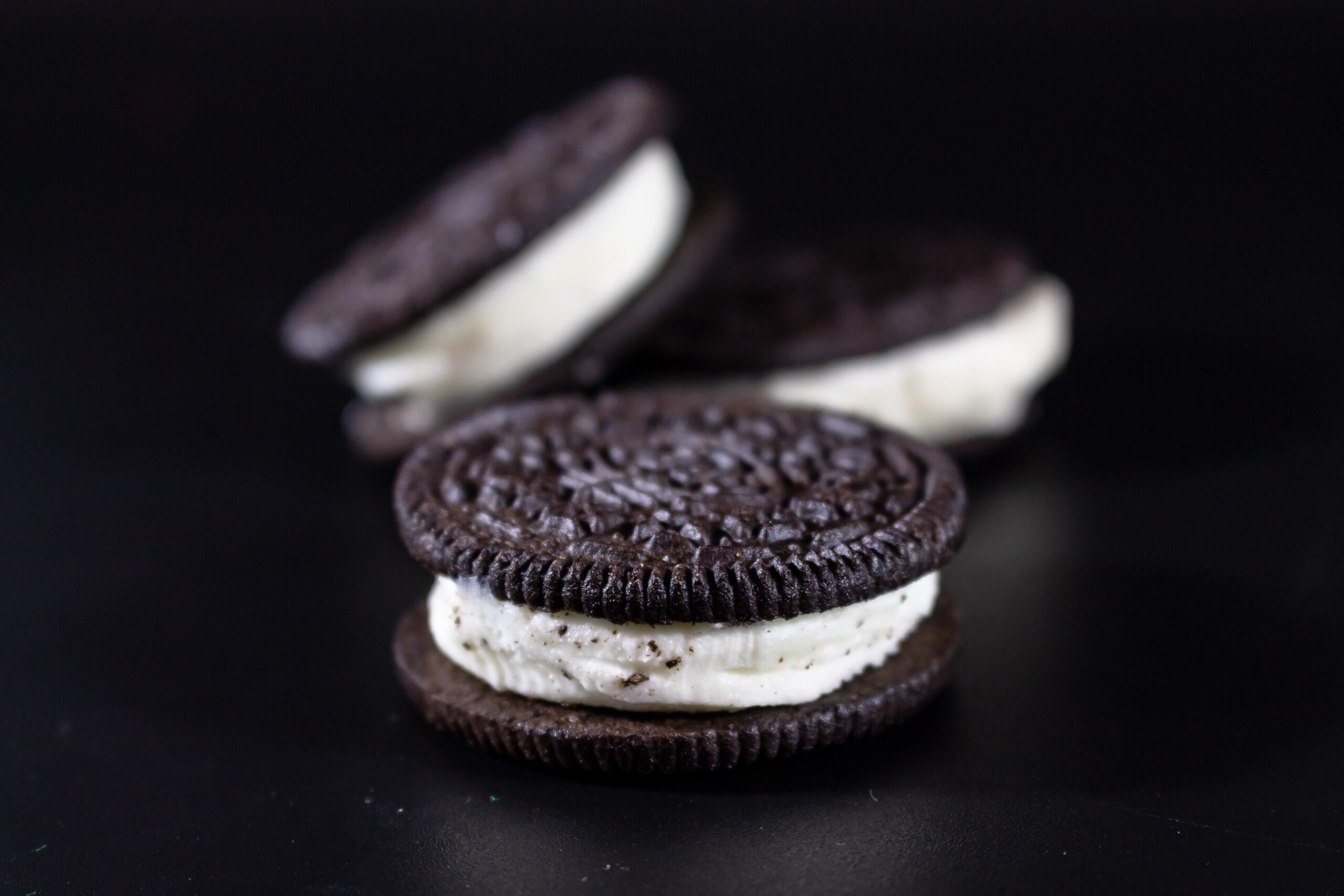 Closeup of one Oreo Big Stuf cookie with two Oreo Big Stuf cookies blurred in the background behind it, all on a black background
