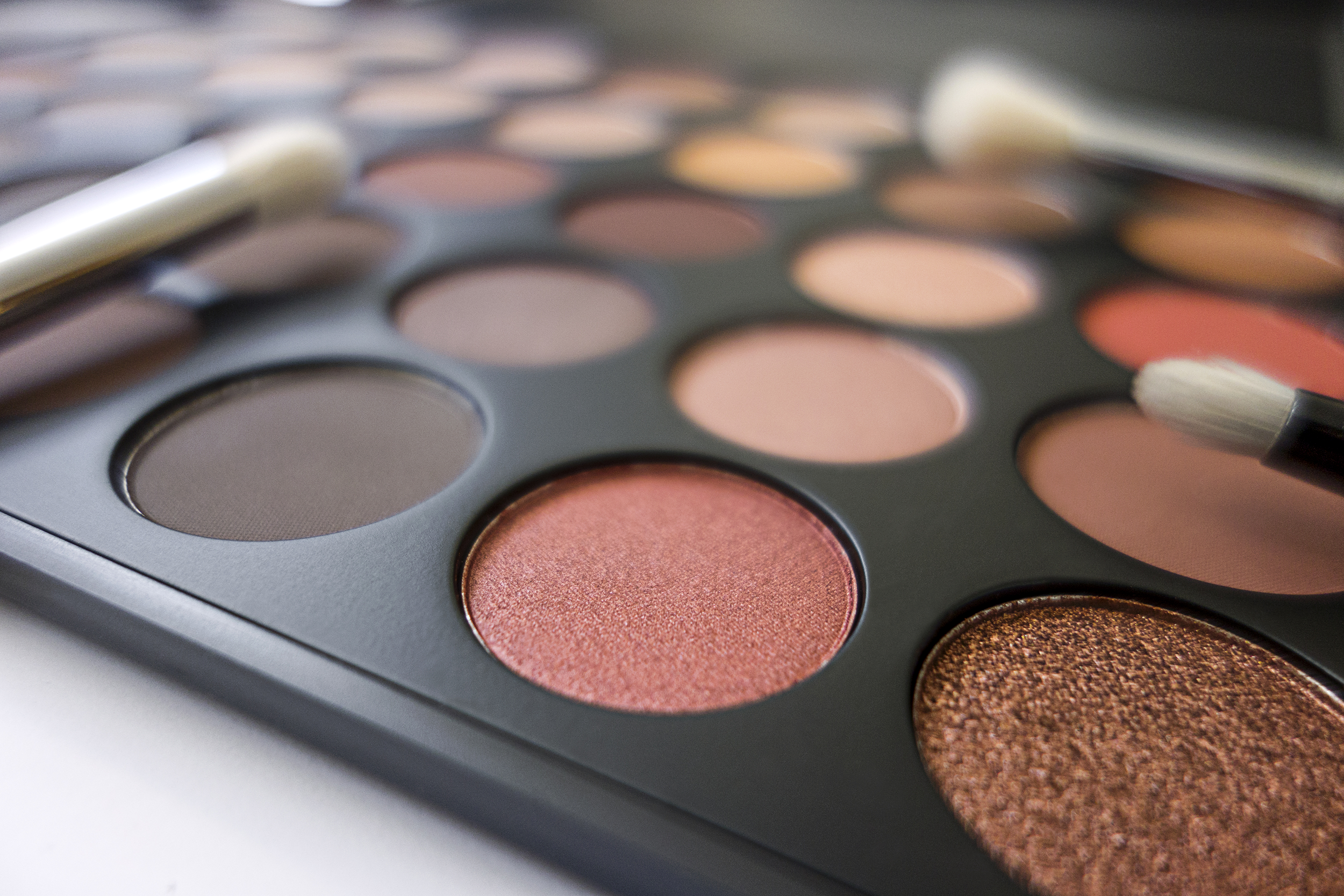 Closeup of blush-pink colors of round eye shadows in a palette, selective focus on colors in the foreground, more round eye shadows blurred in the background