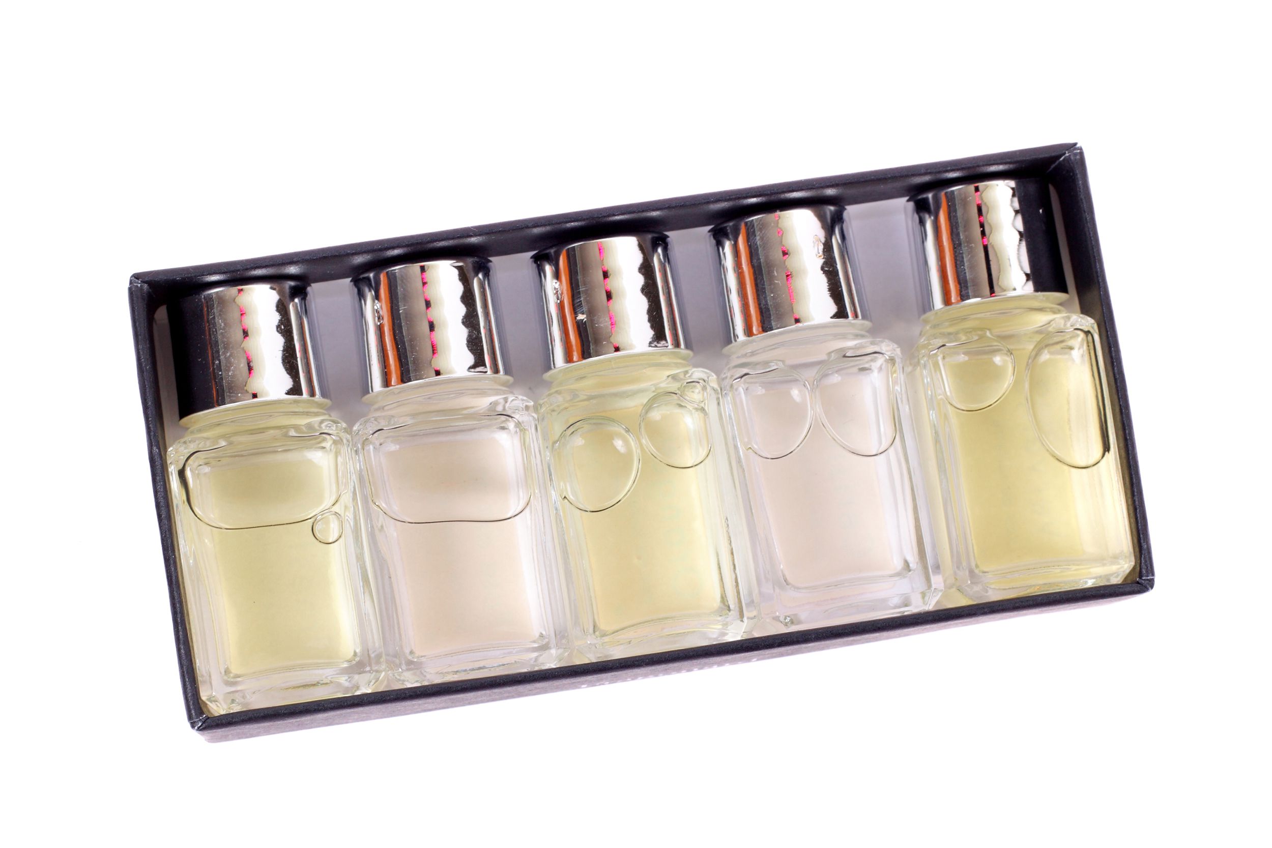 Five small glass bottles in a gift box, light yellows and clear, perfume sampler, on a white background