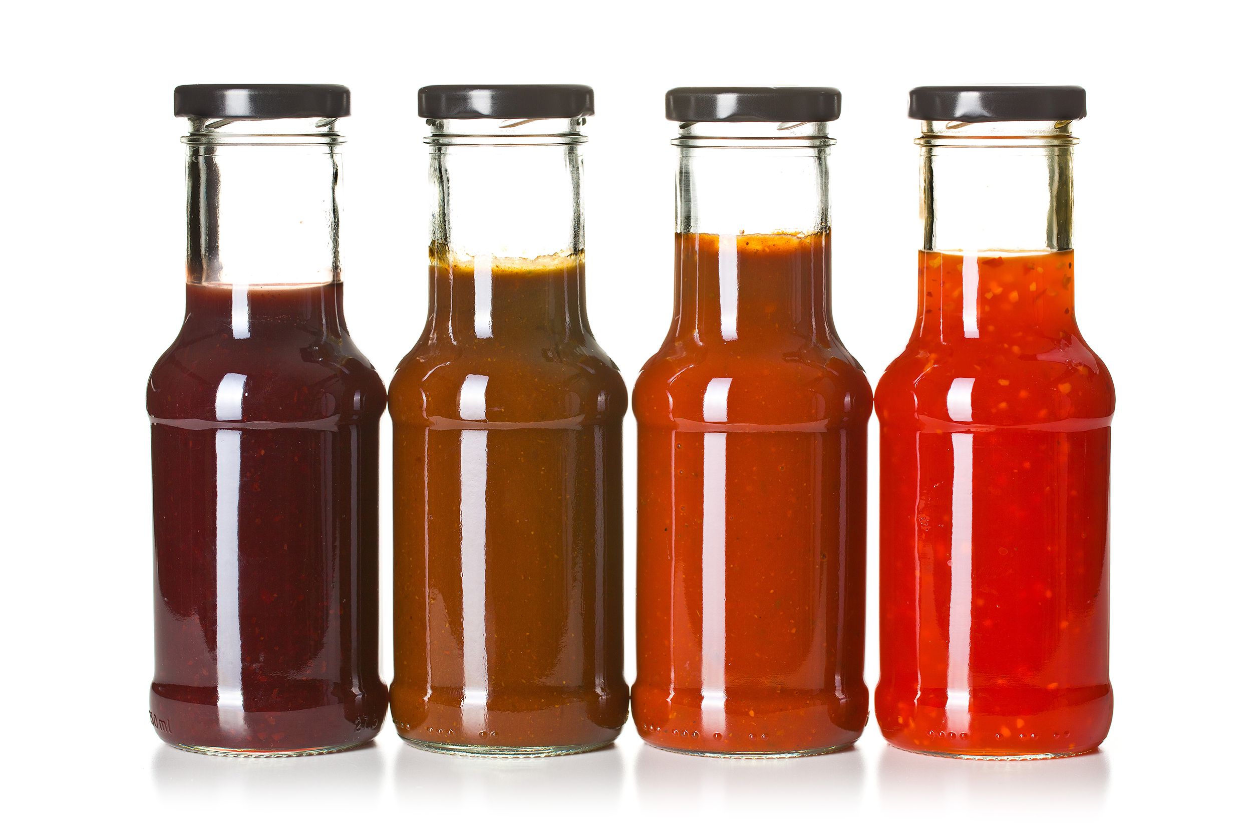 Four small glasses of hot sauce in a line, from dark red to bright red, on a white background